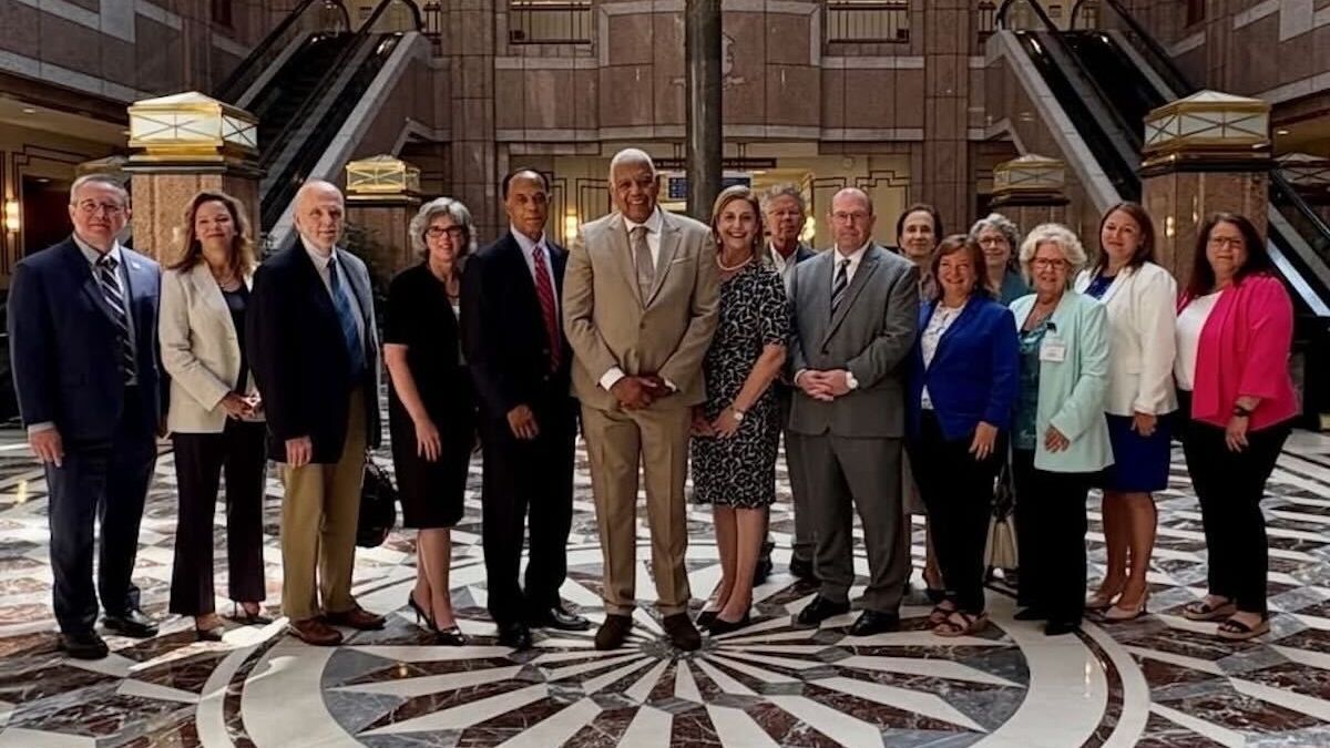 Group of people standing in a grand lobby with a patterned marble floor and staircase background