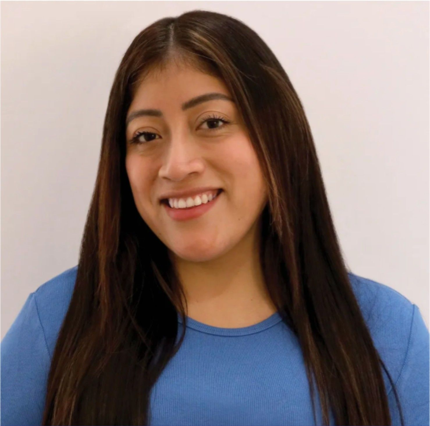 Smiling person with long dark hair wearing a blue shirt against a light background