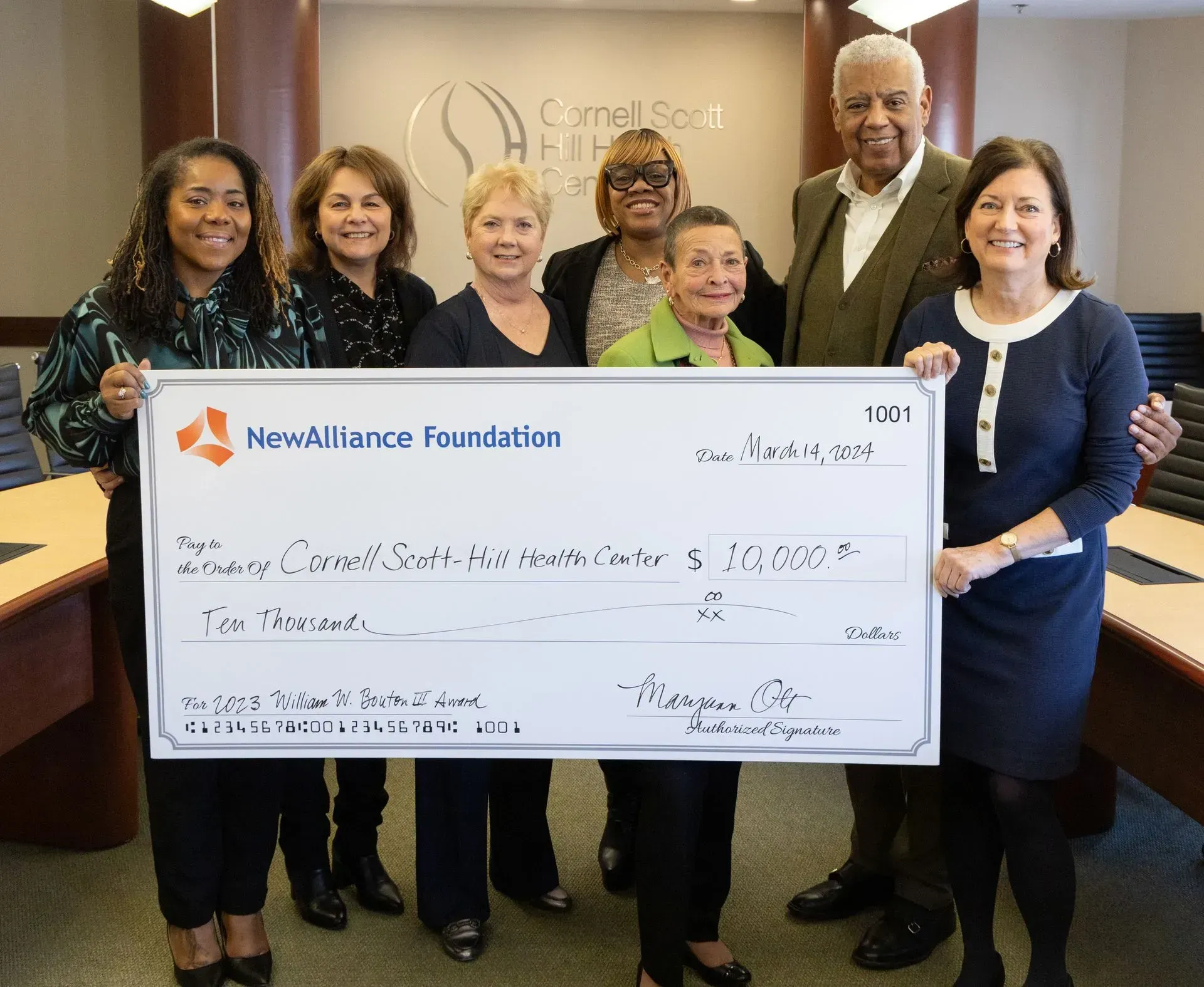 Group holding large ceremonial check in office lobby, smiling at camera.