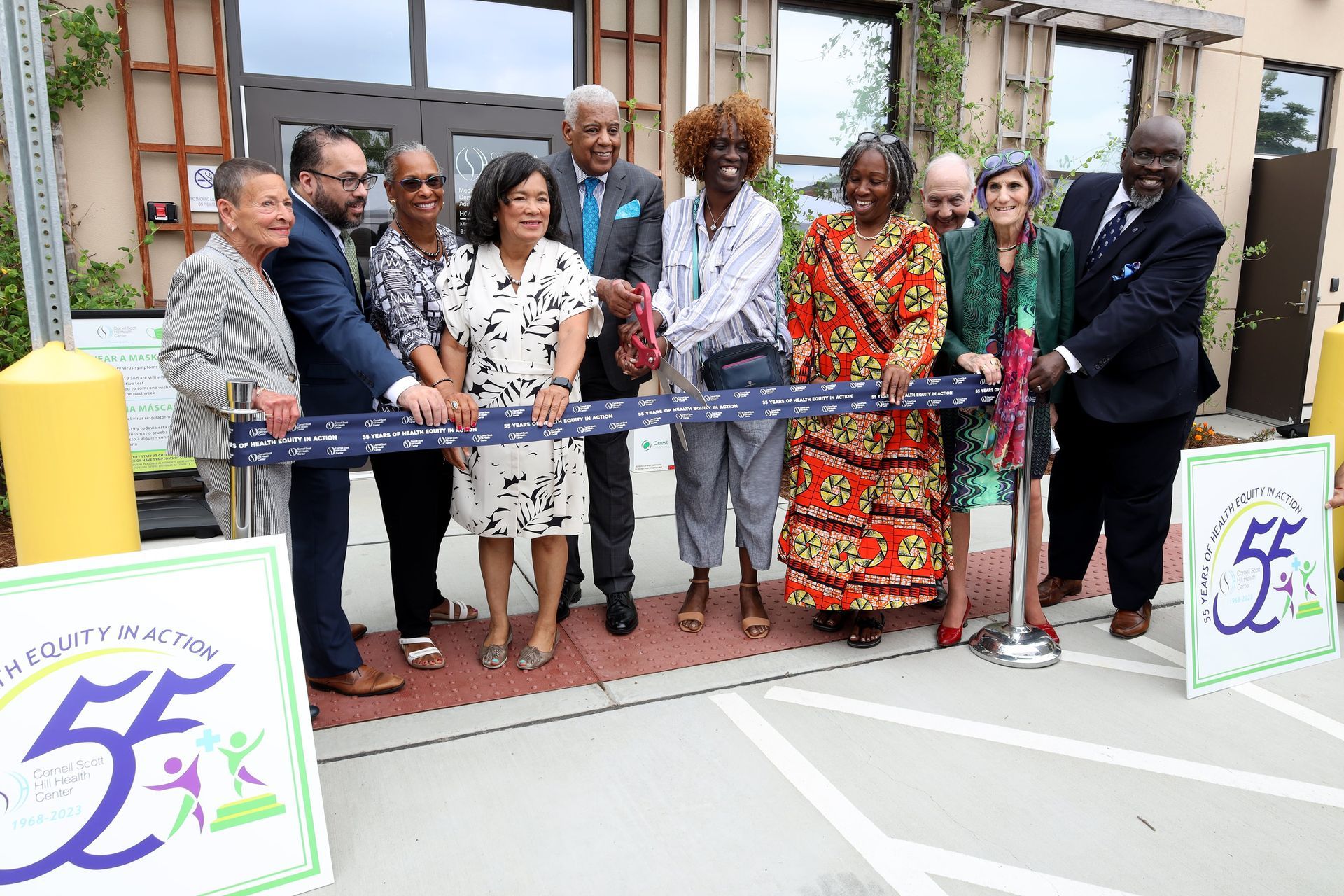 Ribbon-cutting ceremony with a group standing outside a building, holding a blue ribbon and scissors.