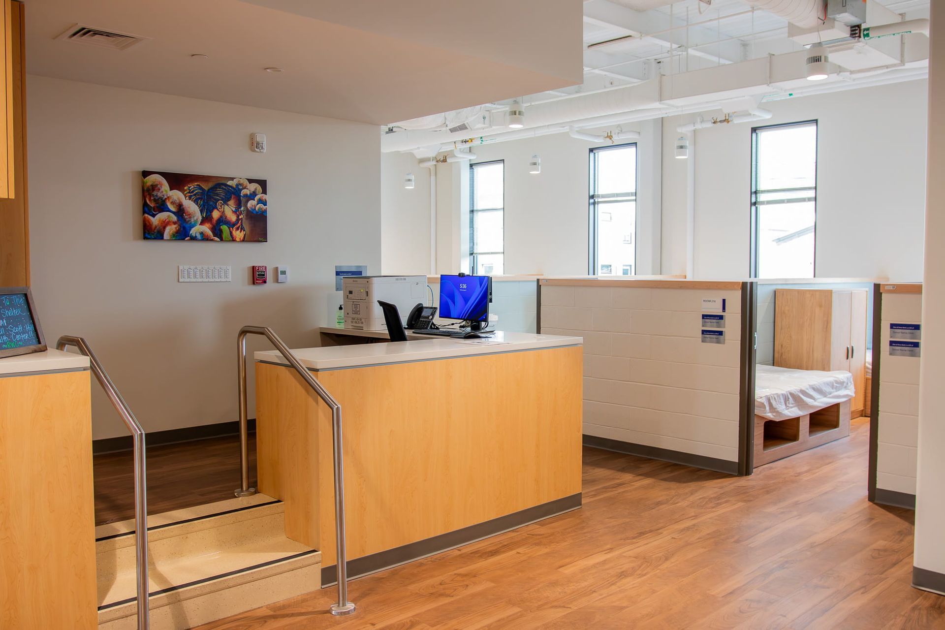 Modern lobby with wood floors, reception desk, seating nook, and bright windows