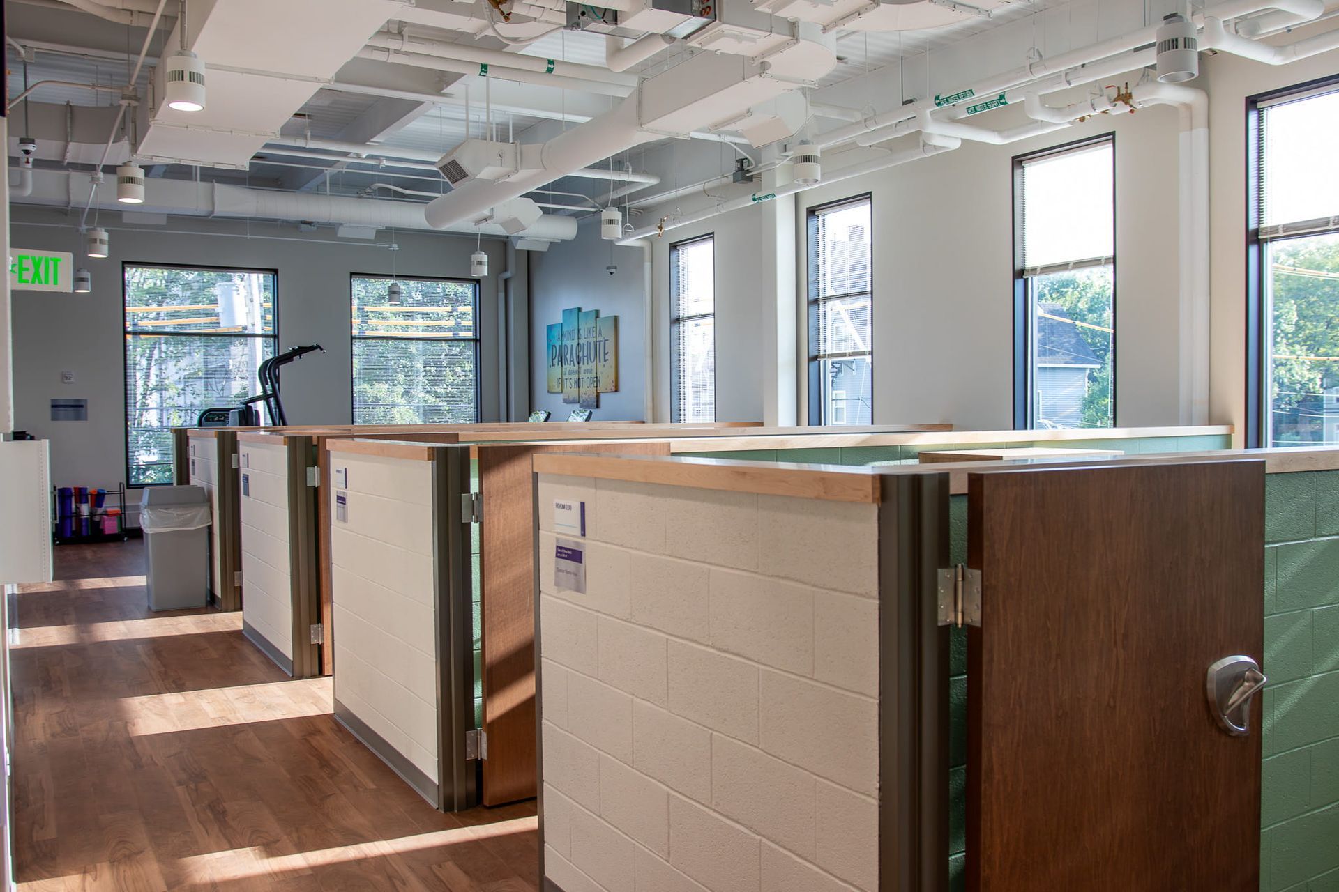 Open office interior with cubicle partitions, wood floors, large windows, and overhead lighting