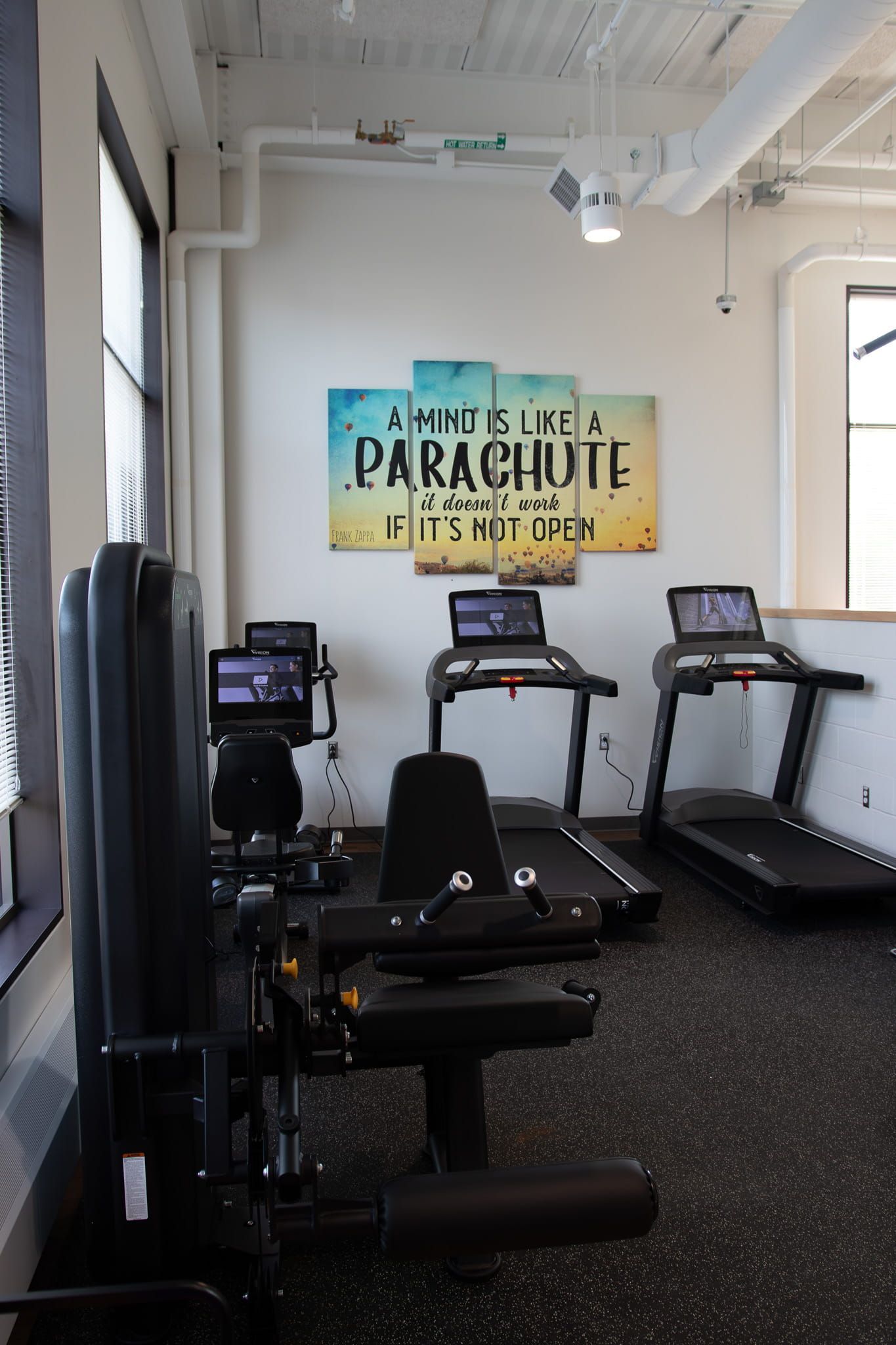 Gym with three treadmills, a seated exercise machine, and a wall sign reading “Live the Parachute Life.”