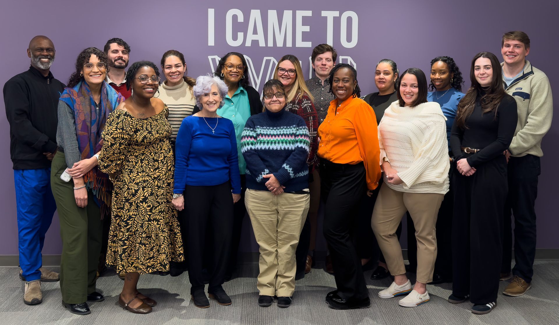Recovery and Wellness Team posing indoors in front of a purple wall with the words “I CAME TO” behind them.