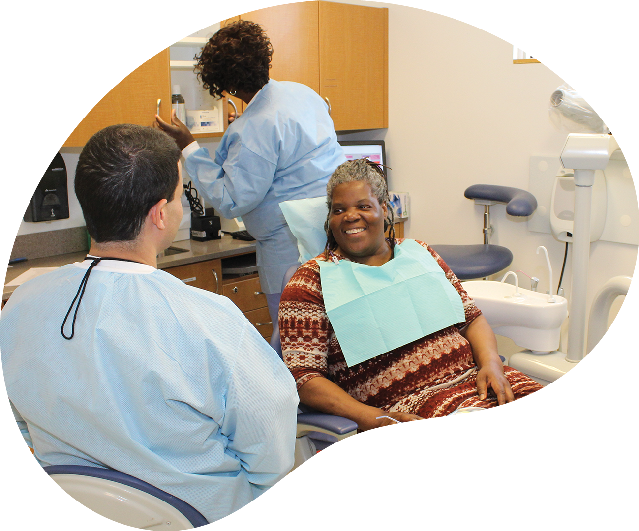 Dental clinic with patient smiling in chair while two staff members work nearby