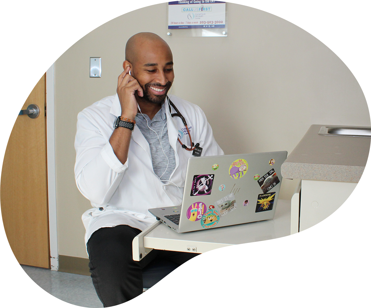 Doctor smiling while talking on the phone beside a laptop in a clinic office