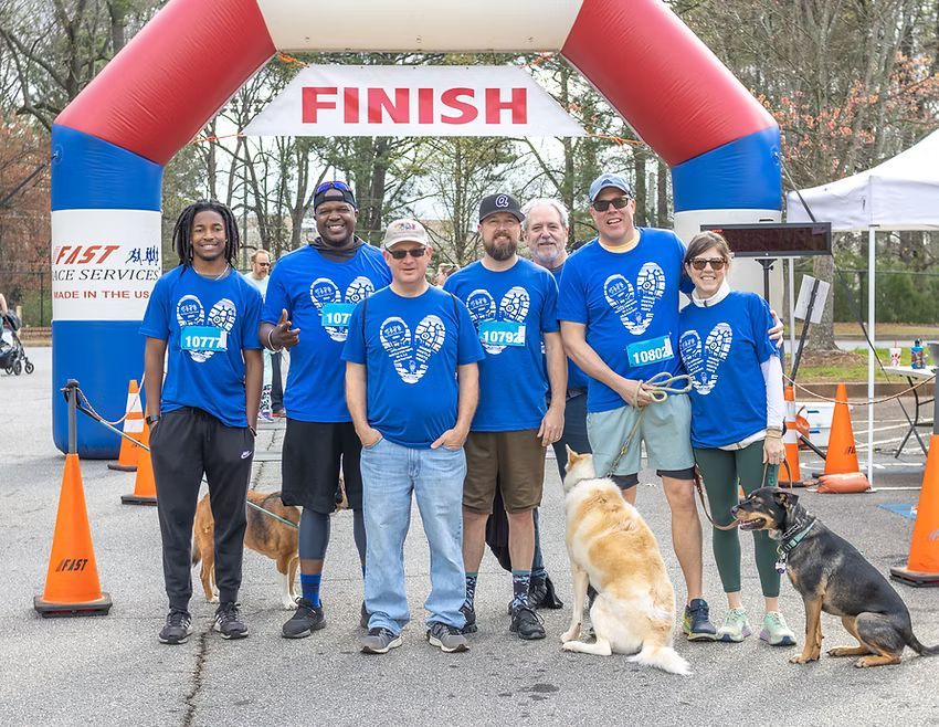 Group of people in blue shirts stand under a finish line archway with dogs.