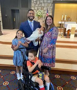 Family posing for a photo in a church after a baptism; includes a baby, child in wheelchair, and a daughter.