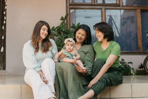 Four people sit on a porch, smiling and holding a baby in a green dress.