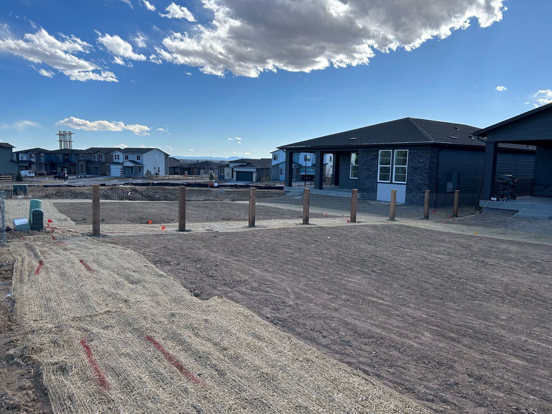 Construction site with gravel lot, wooden posts, and a dark-roofed building under a cloudy blue sky