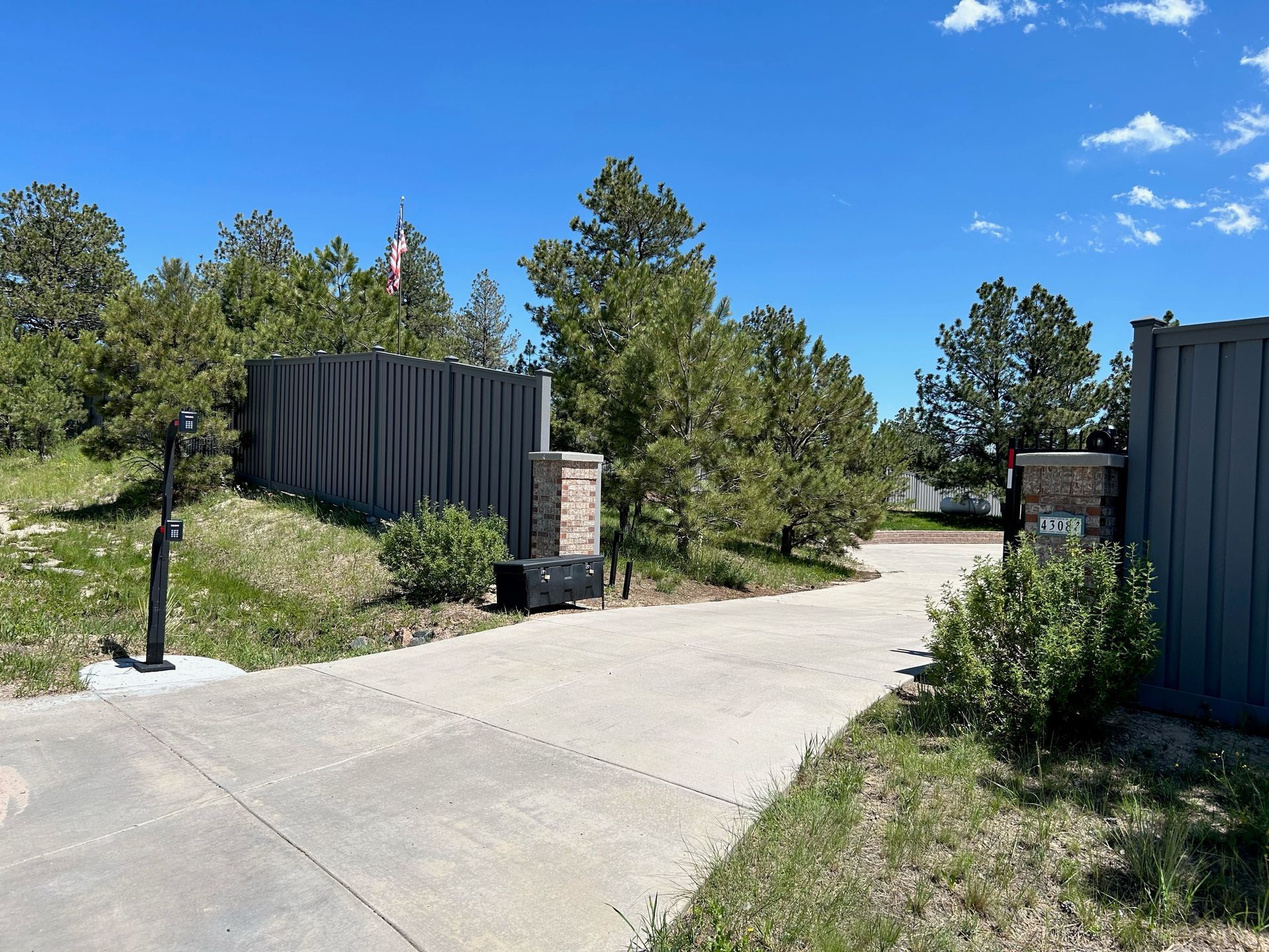 Concrete path between dark corrugated walls and trees under a bright blue sky