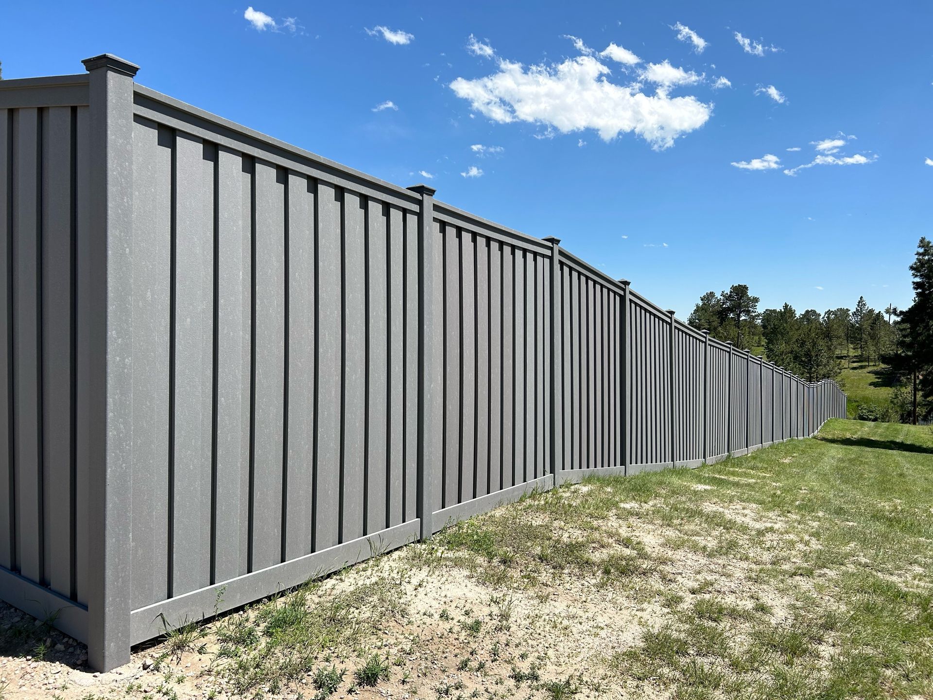 Gray metal fence along a grassy yard under a blue sky with clouds