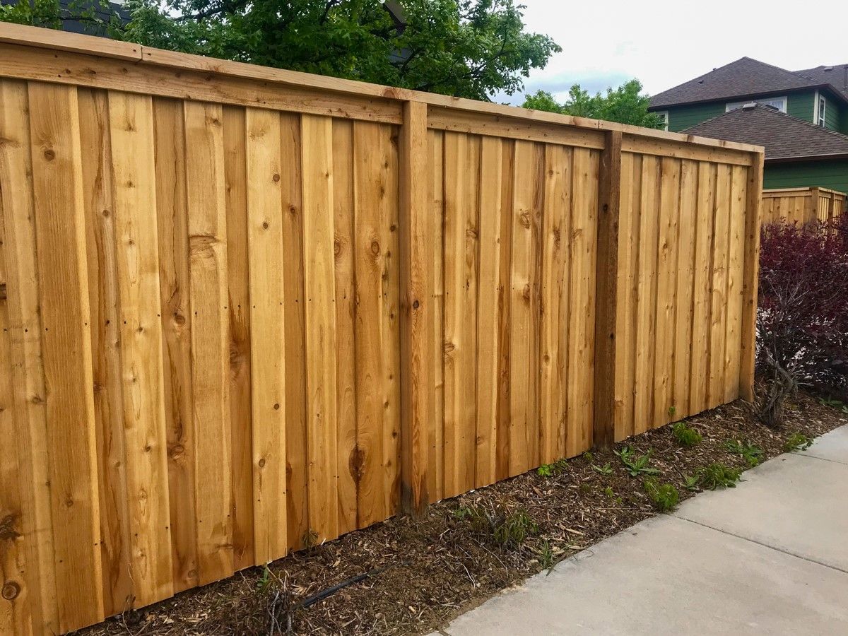 New wooden privacy fence along a sidewalk with houses and trees in the background