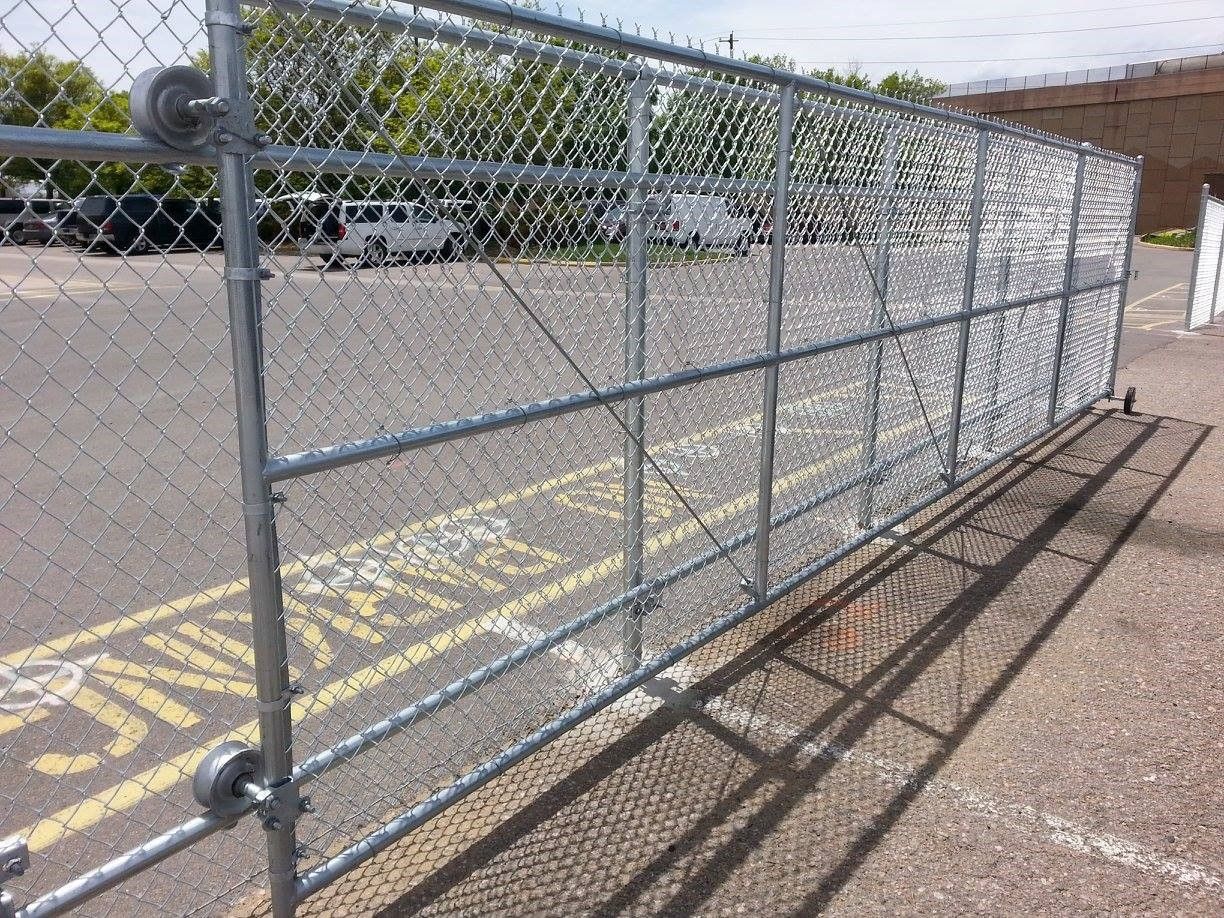 Chain-link fence and gate blocking a painted parking area beside a building, with long shadows on pavement