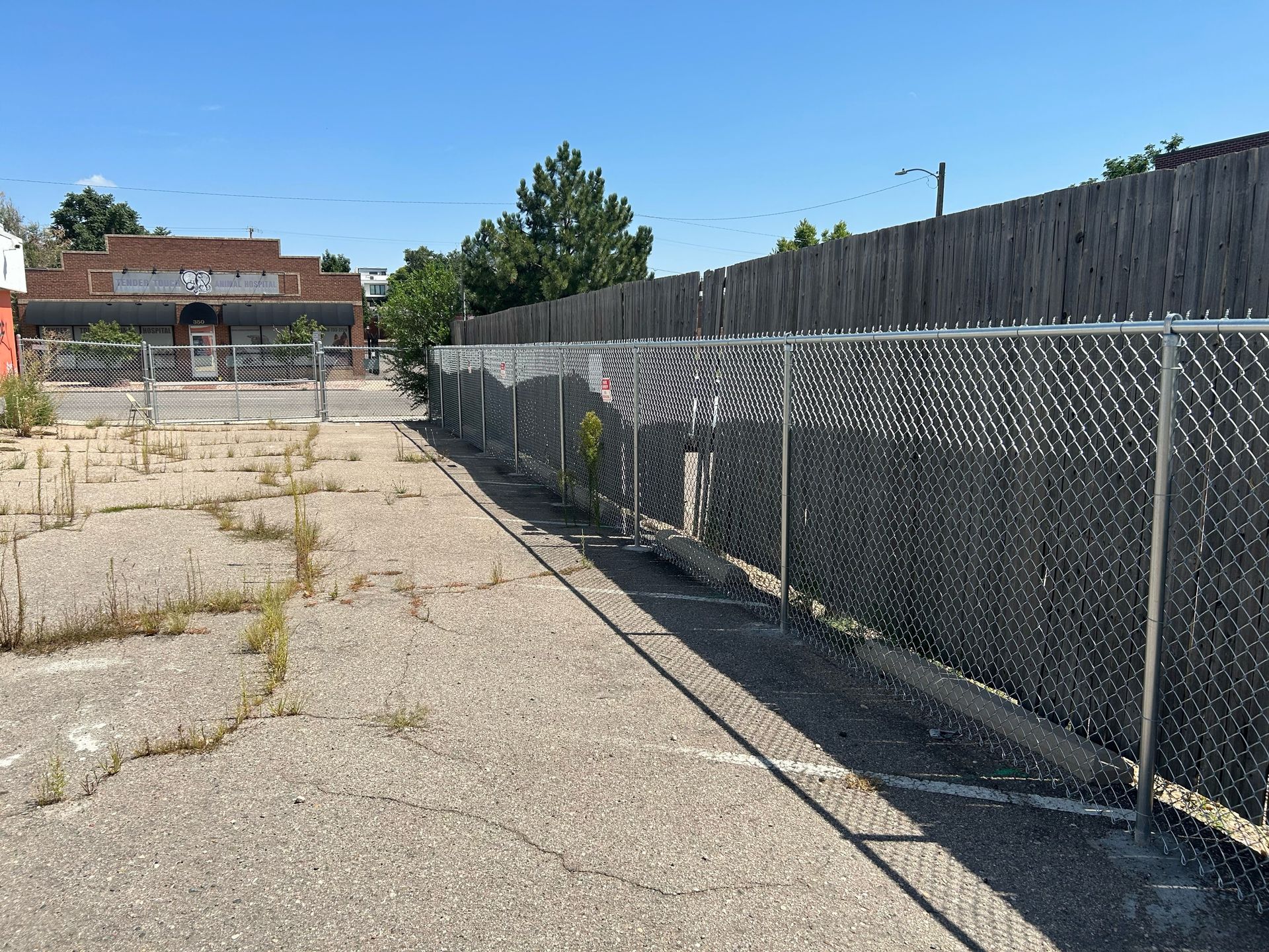 Empty cracked lot beside chain-link fence under a clear blue sky