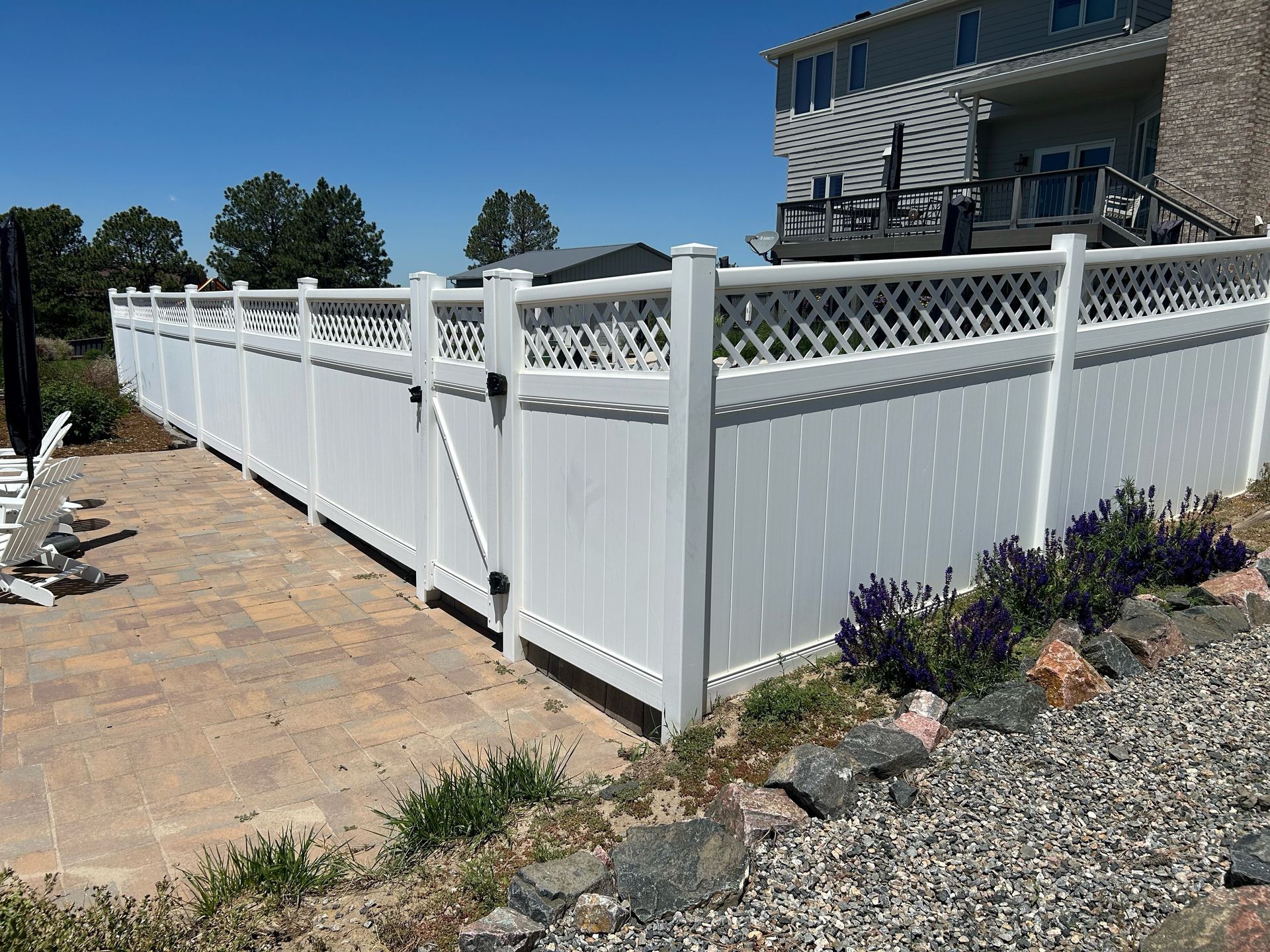 White vinyl fence with lattice top beside a stone patio and house in a landscaped yard