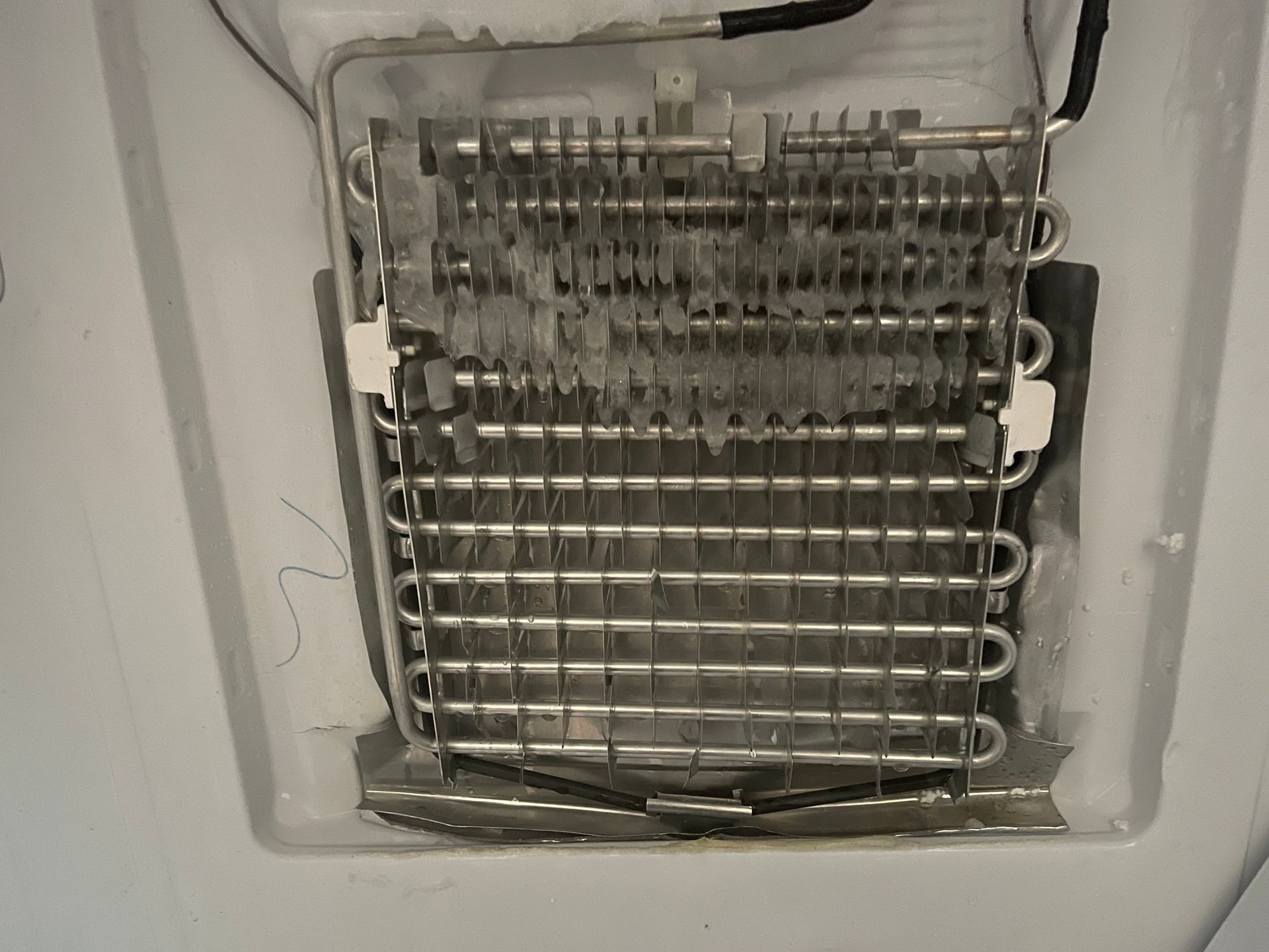 A refrigerator's evaporator coil, covered in frost, inside the freezer compartment.