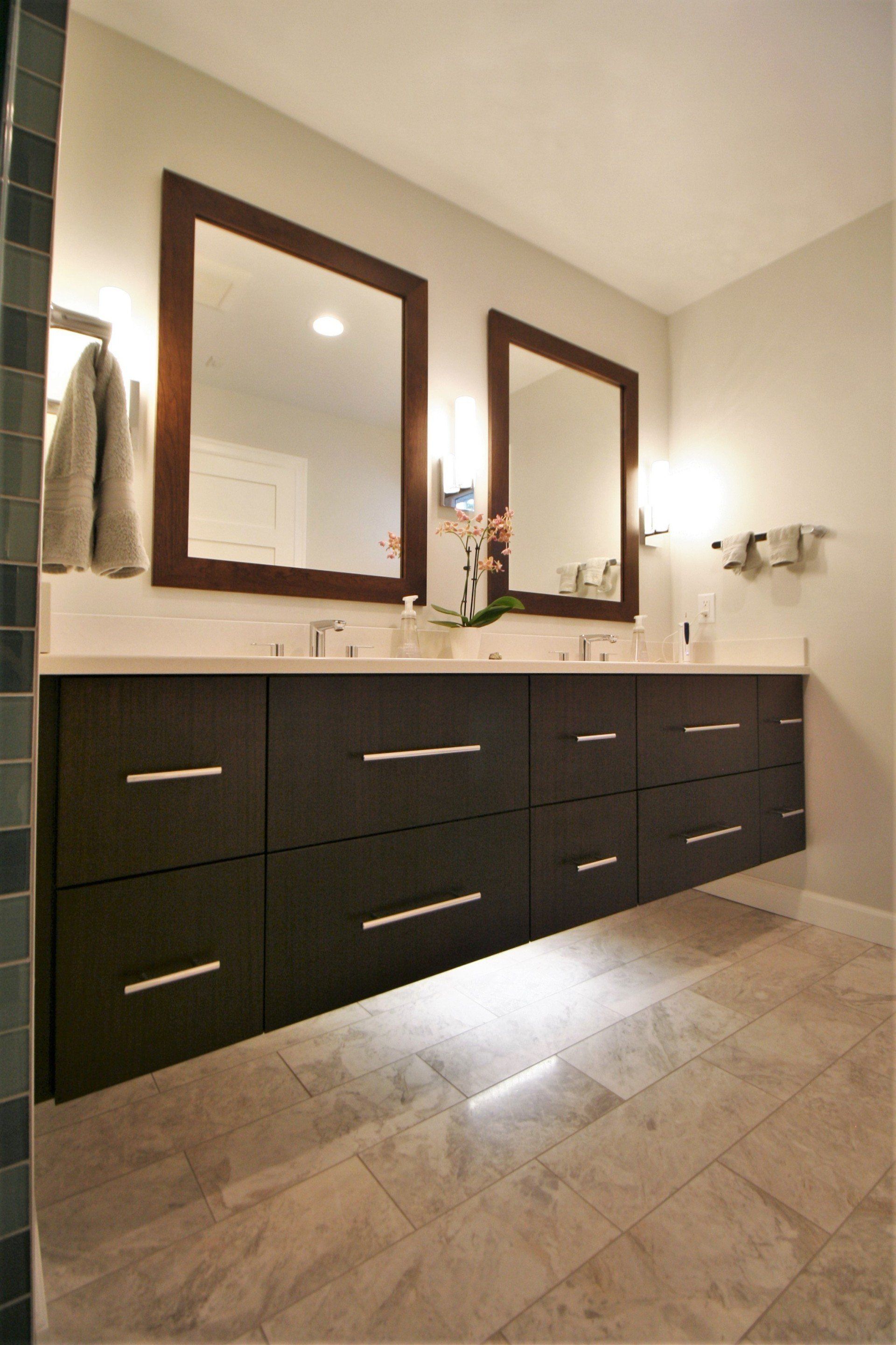 Modern bathroom vanity with dark cabinets, double mirrors, and wall sconces on beige tile floor