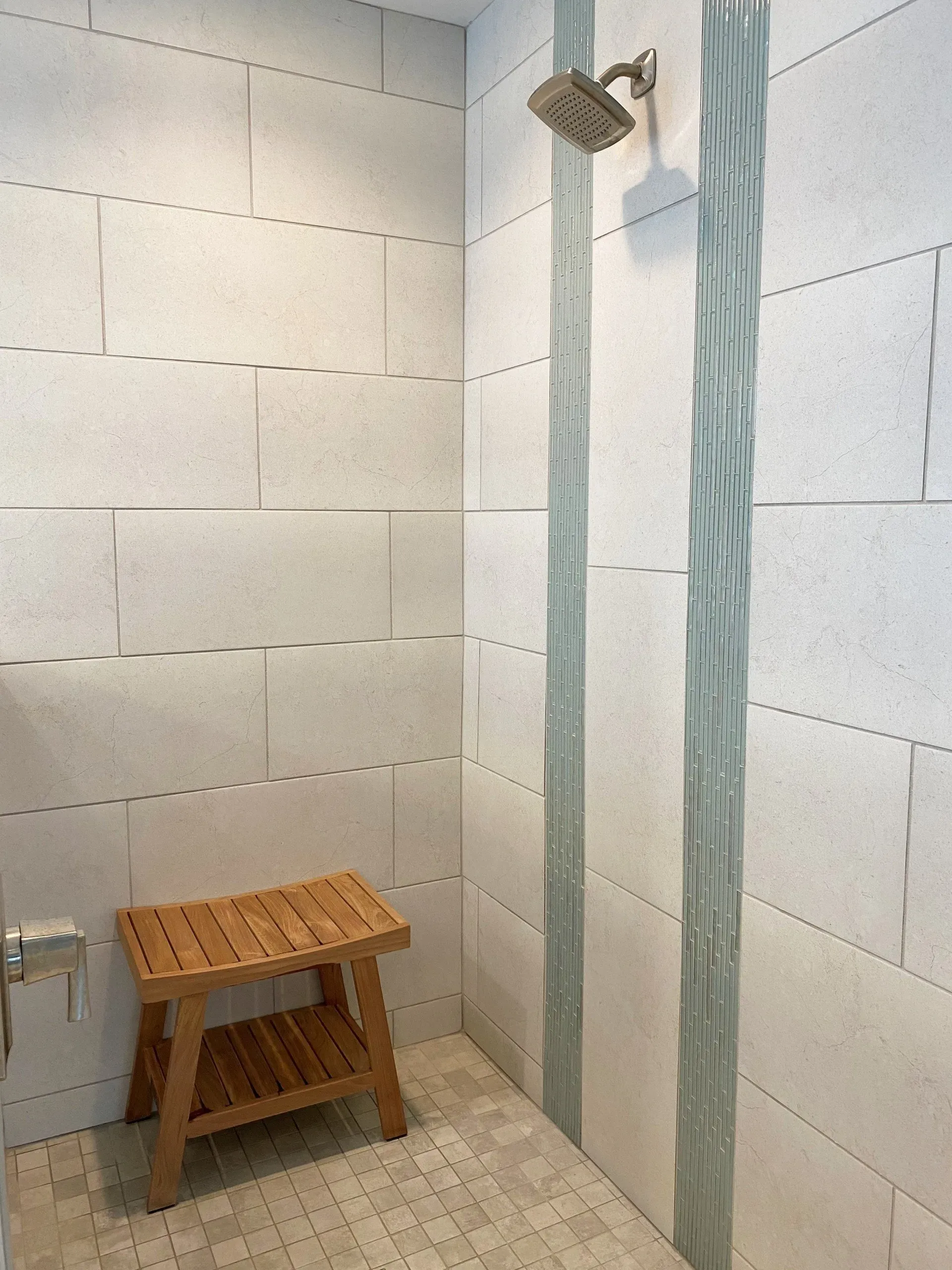 Small tiled shower stall with a wooden stool and a hanging shower curtain