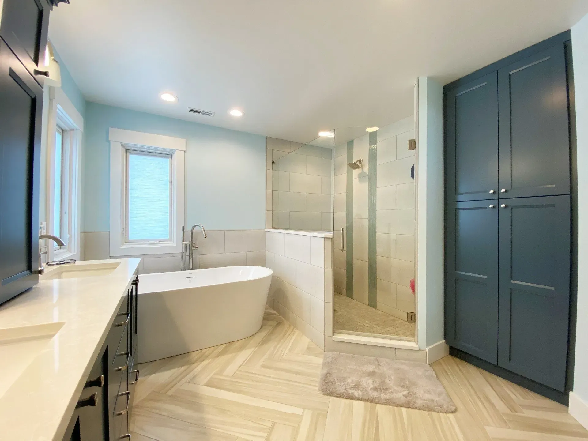 Bright modern bathroom with a freestanding tub, glass shower, and dark built-in cabinets