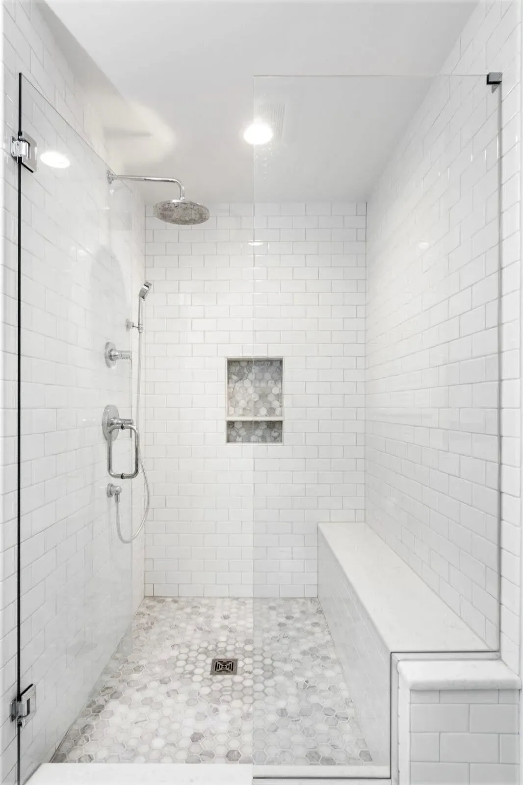 Bright white tiled walk-in shower with glass door, rainfall showerhead, and built-in bench.