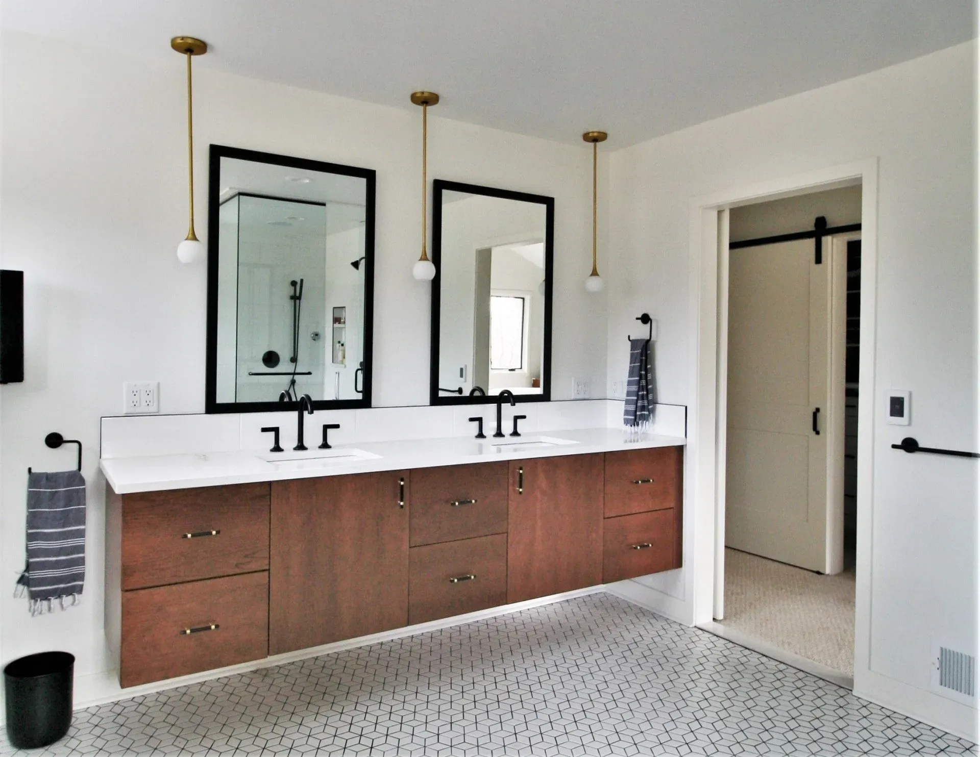 Modern bathroom with double vanity, two mirrors, brass lights, and white hex tile floor.