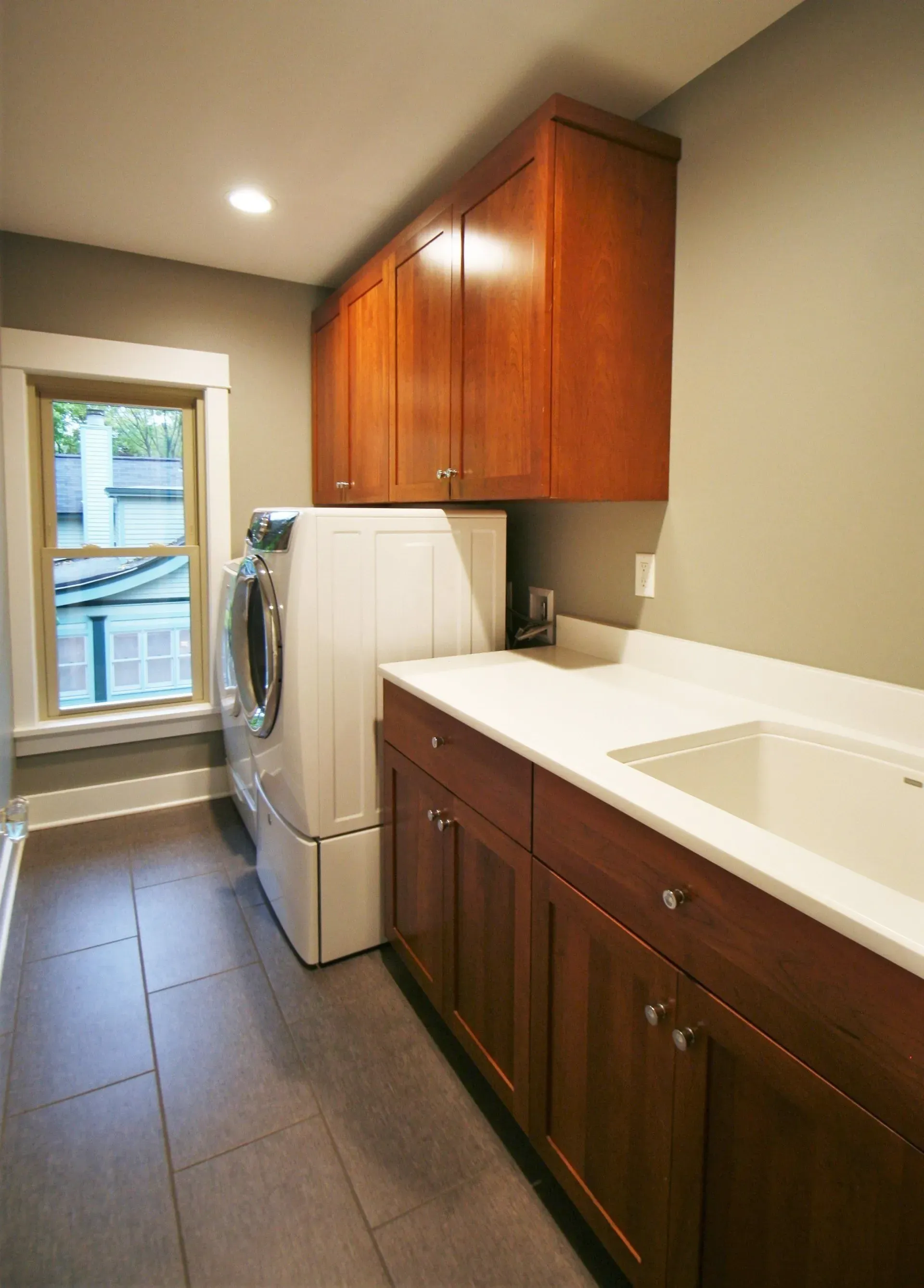 Laundry room with white washer and dryer, dark wood cabinets, and a utility sink by a window.