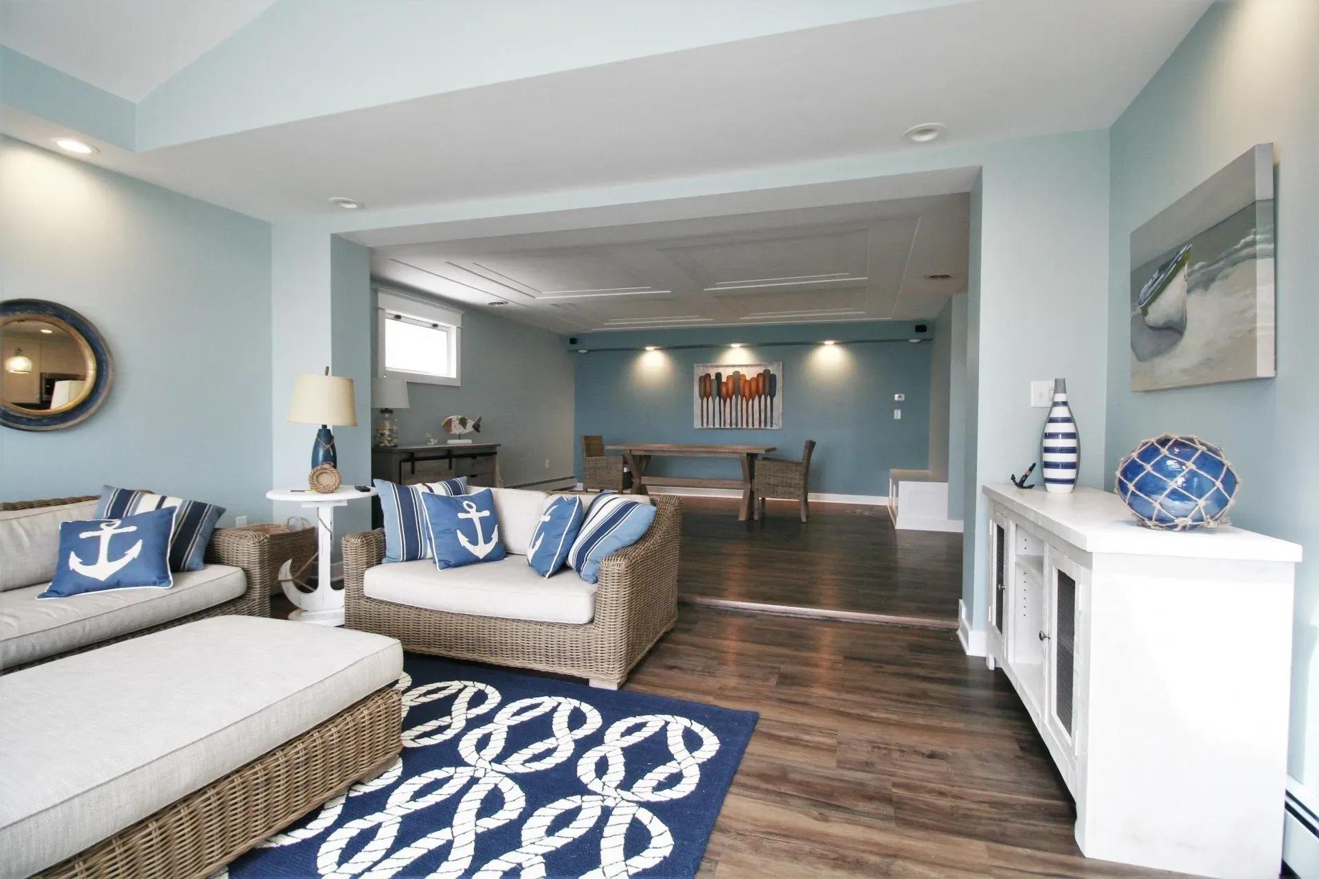 Bright coastal-style living room with blue-and-white decor, sectional sofa, rug, and open dining area