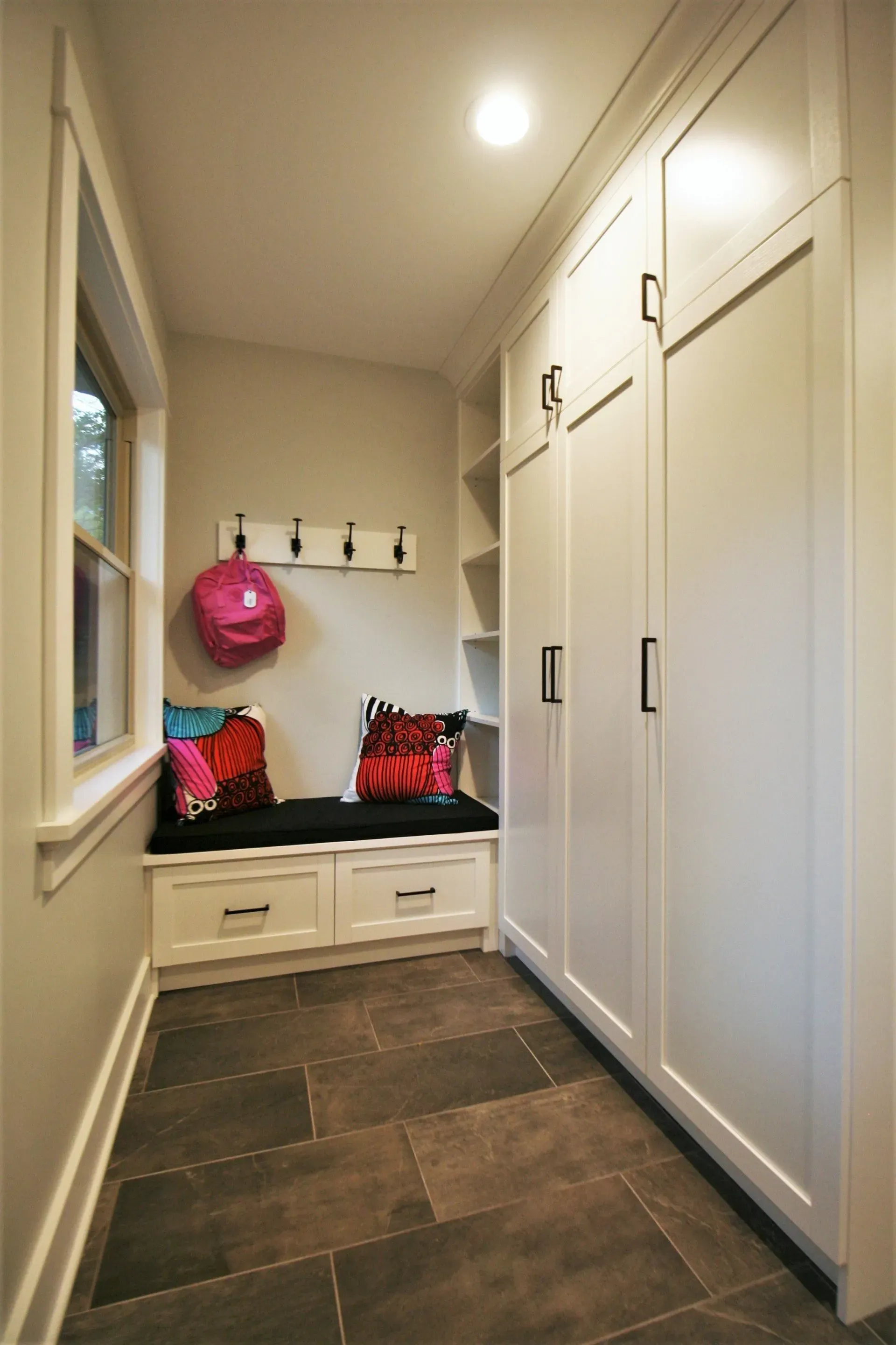 Narrow entryway with built-in white storage, a bench with cushions, and dark floor tiles.