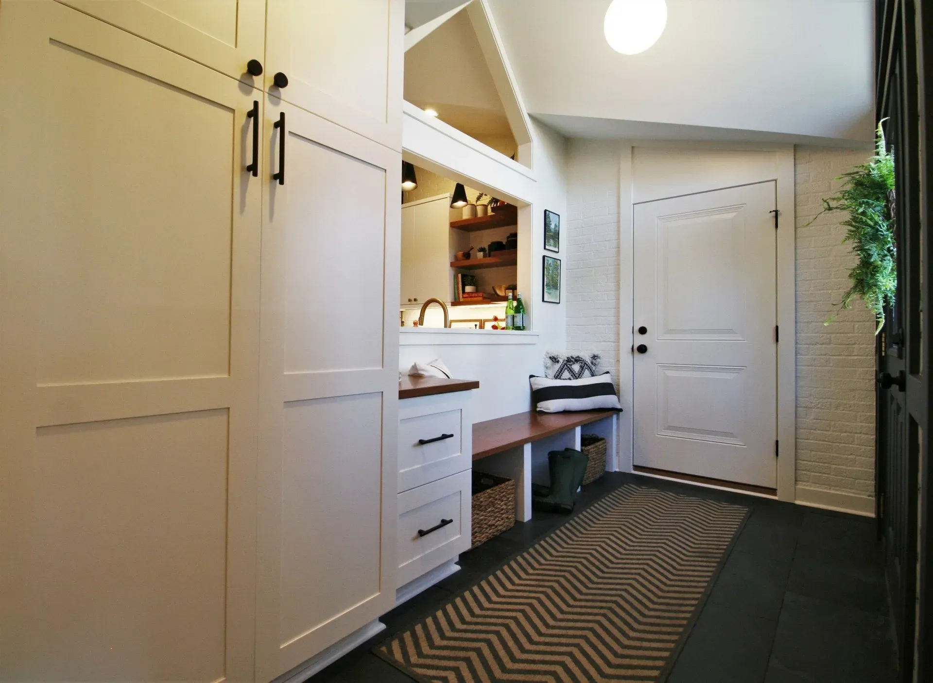 Bright hallway mudroom with built-in white cabinets, bench, patterned rug, and closed front door.