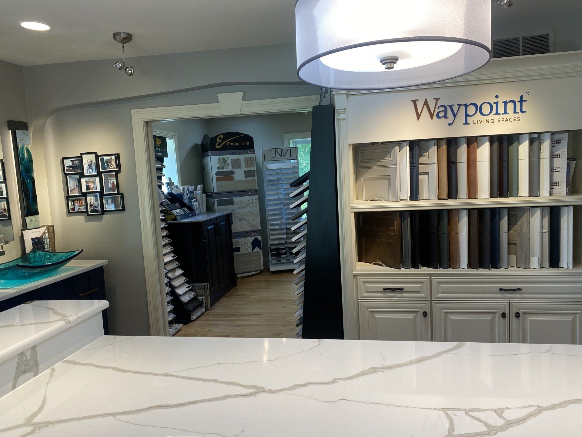 Waypoint showroom with shelves of samples, cabinets, and a large pendant light over a white counter.