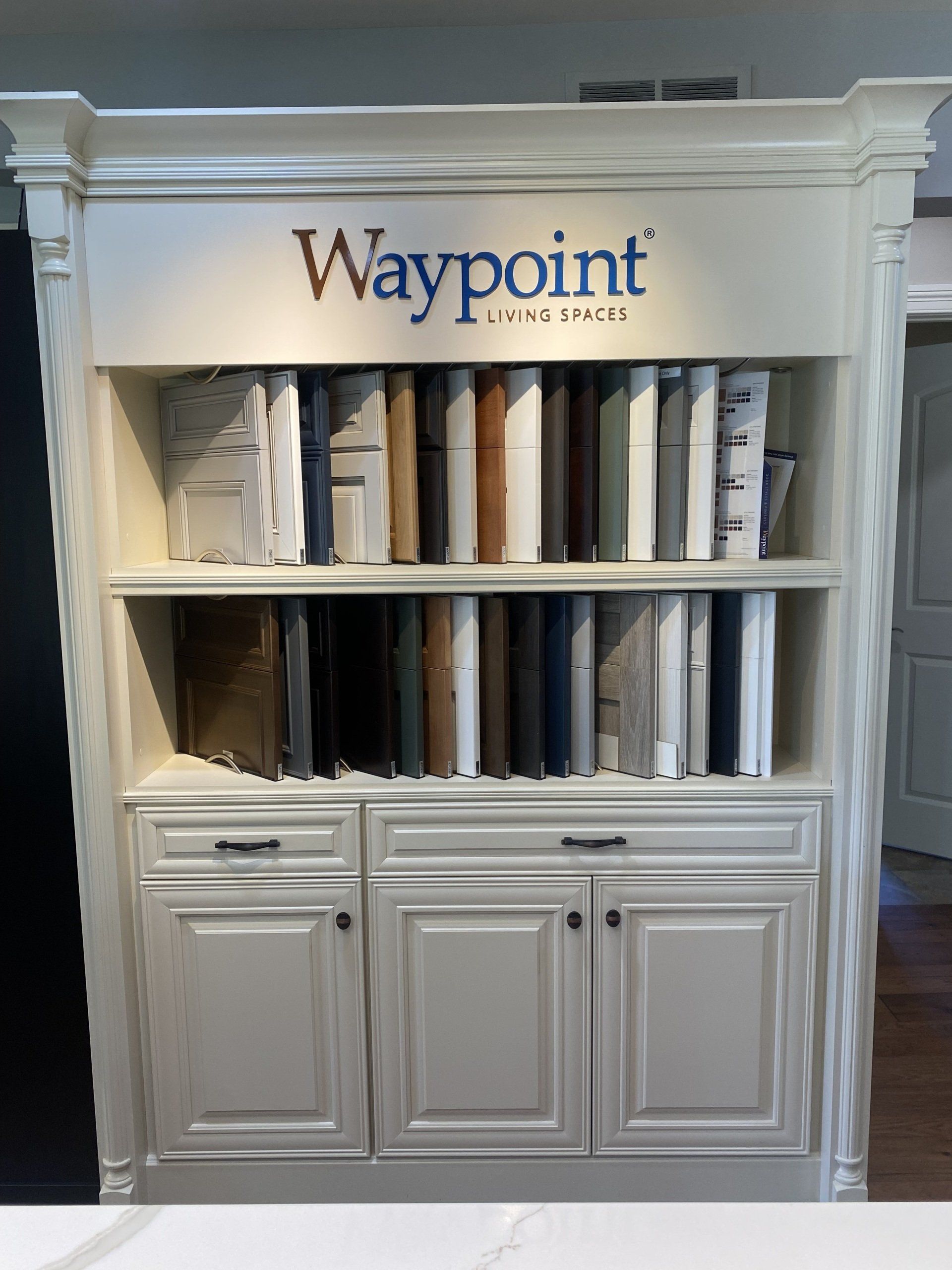 White display cabinet with shelves of rolled materials and a “Waypoint” sign on top