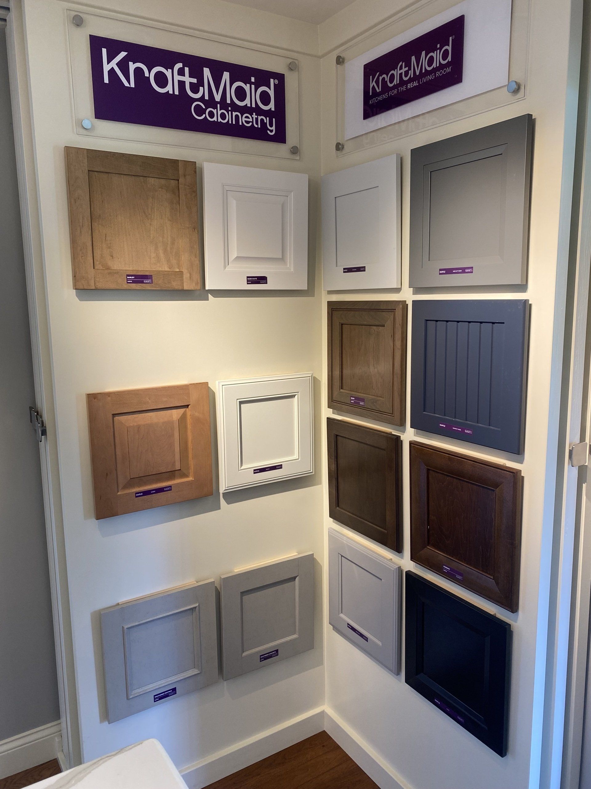 Display of cabinet door samples in a showroom corner, with wood, white, gray, and blue finishes.