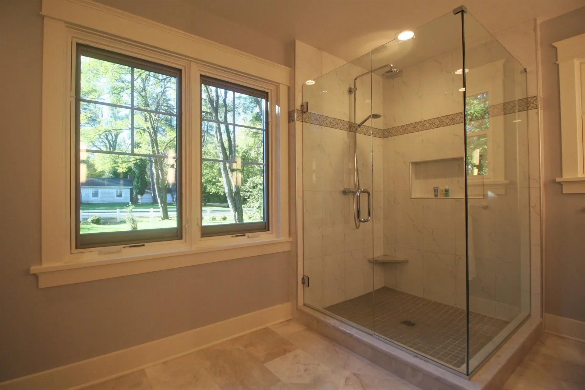 Modern bathroom with large window and glass-enclosed walk-in shower in beige tones