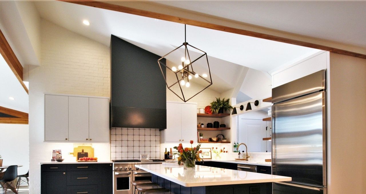 Modern kitchen with white island, black cabinetry, stainless fridge, and geometric pendant light