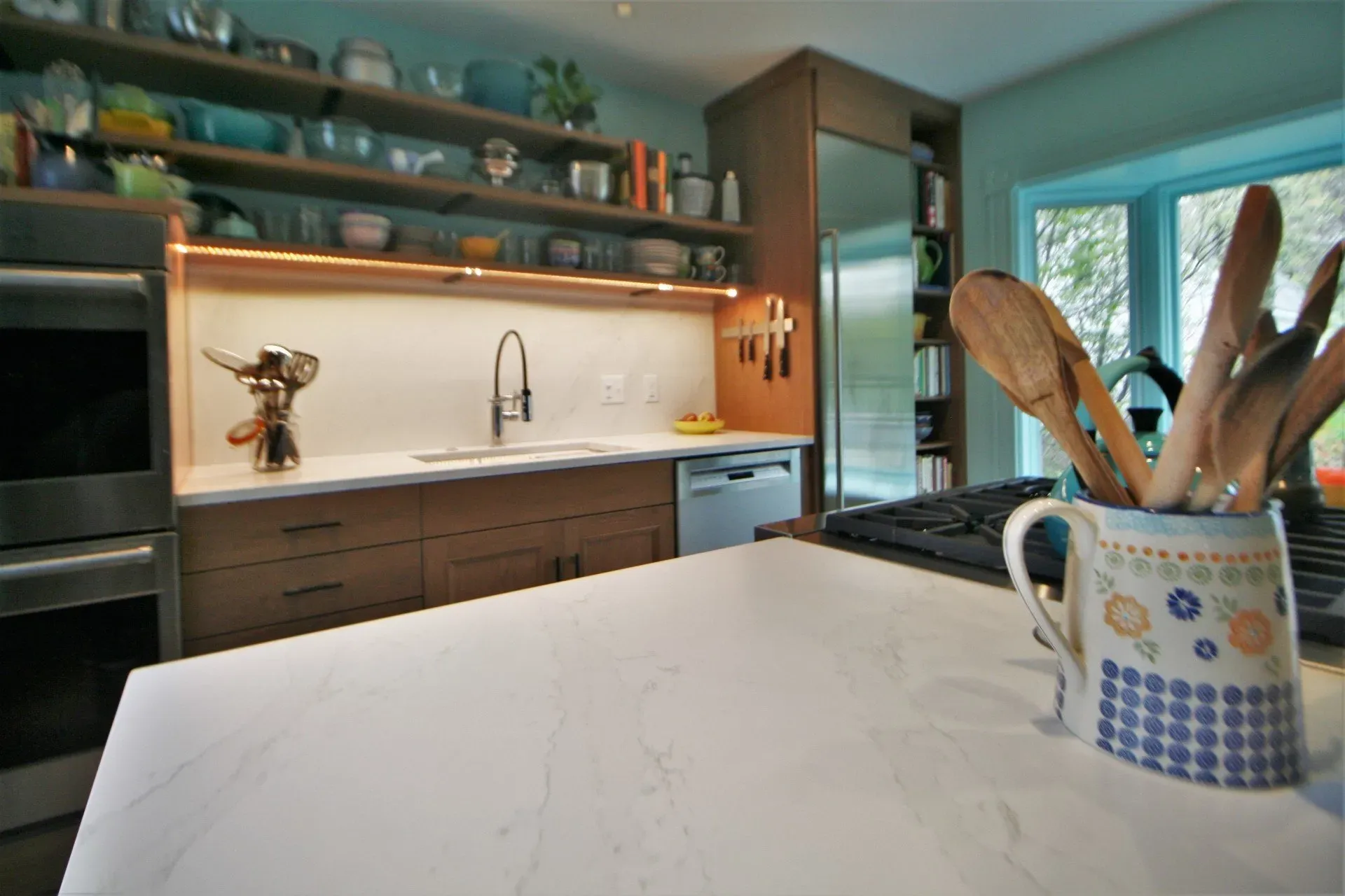 Modern kitchen with white island, dark cabinets, open shelves, and utensil crock by the stove