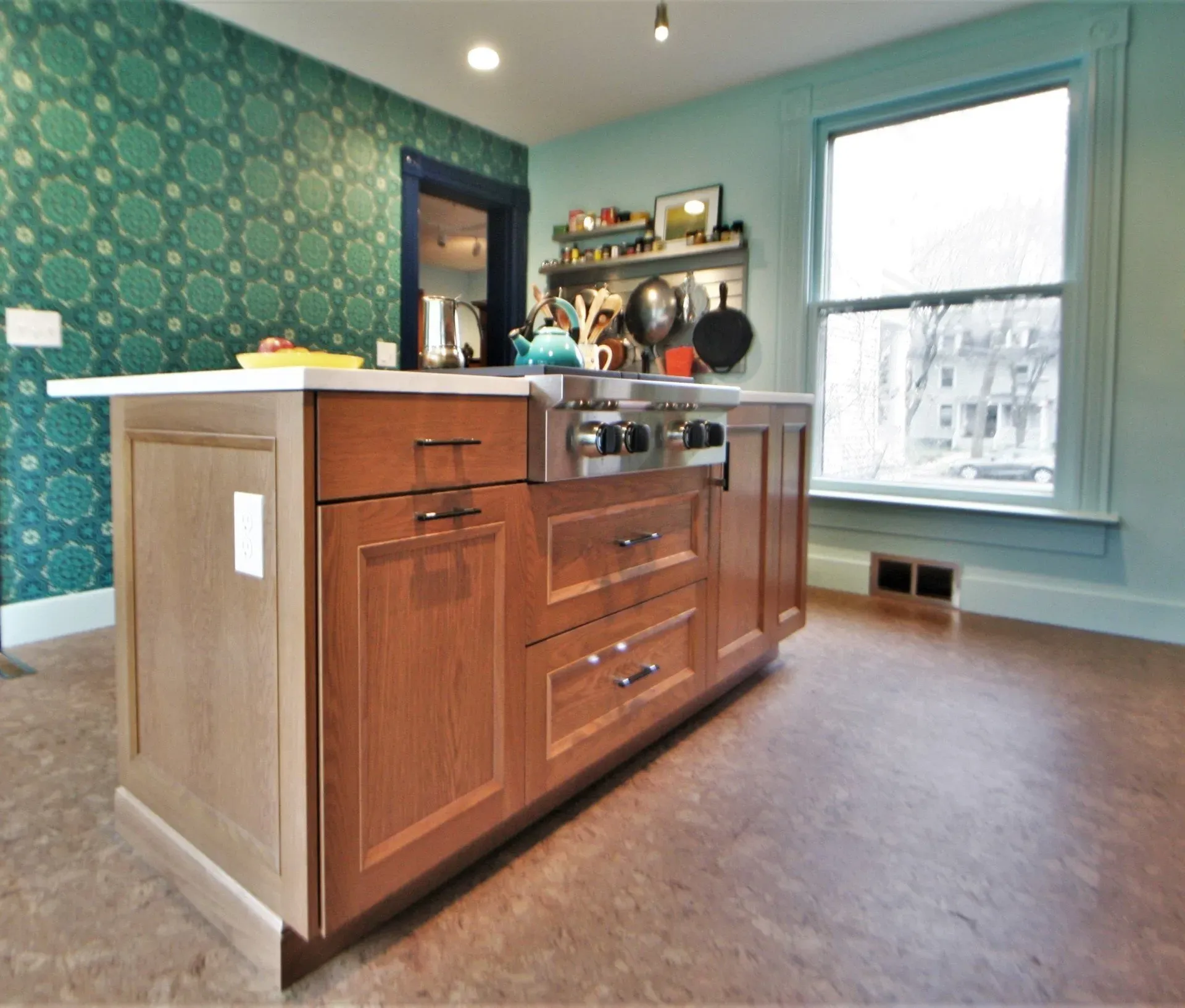 Modern kitchen with wood island, teal patterned wall, and bright window.