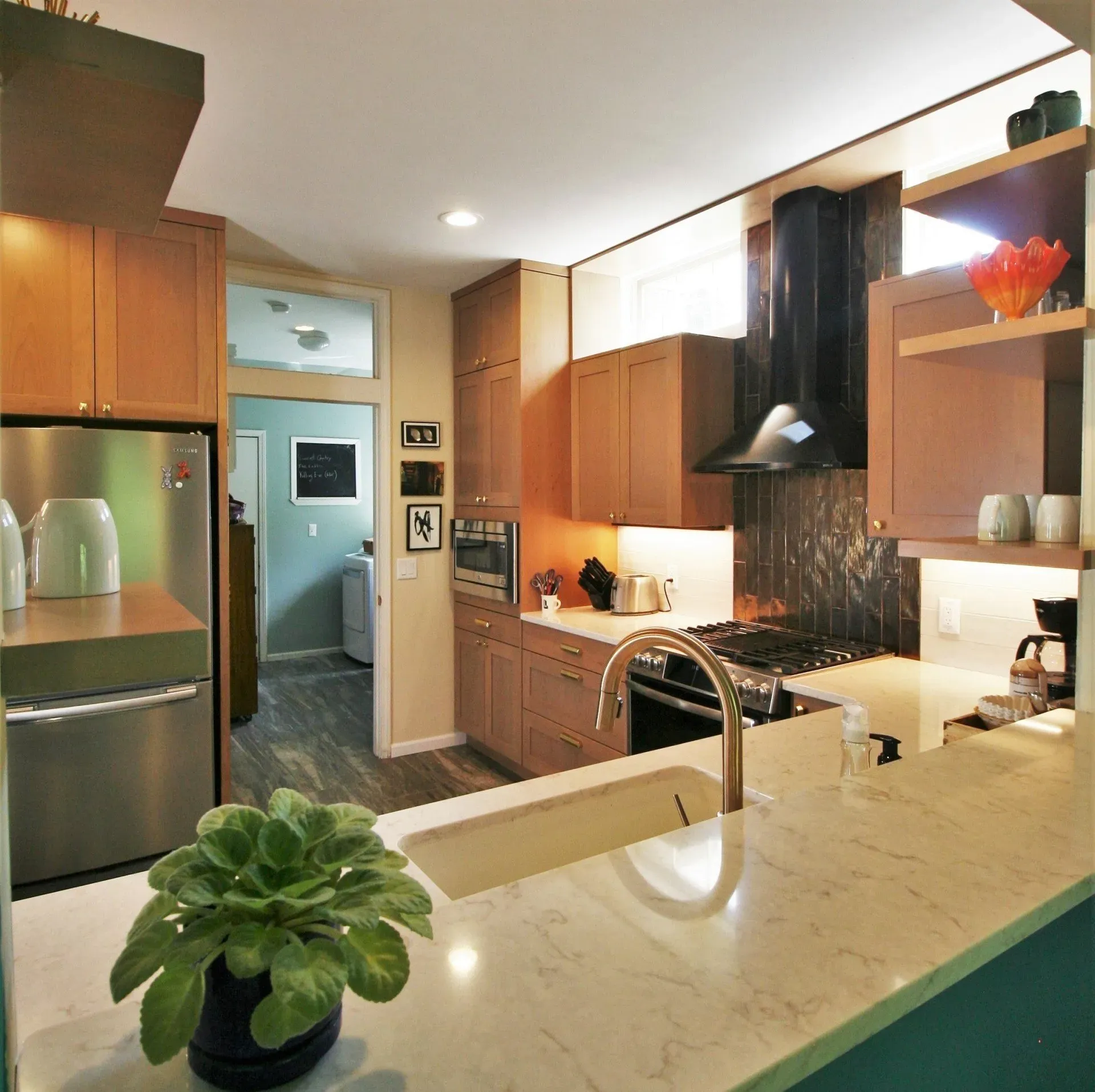 Modern kitchen with wooden cabinets, stainless fridge, marble island, and black range hood