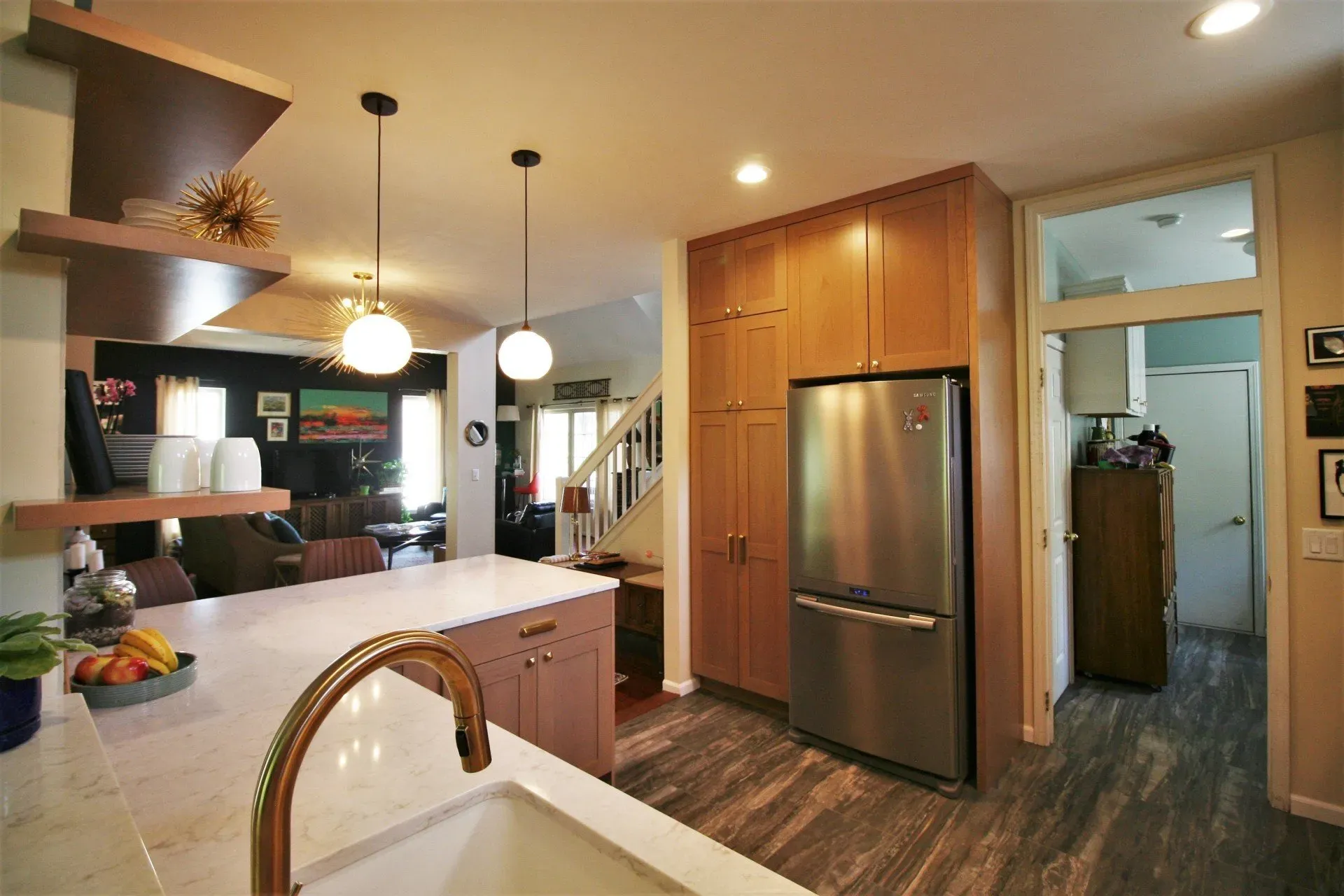 Modern kitchen with stainless fridge, wood cabinets, island sink, and warm pendant lighting