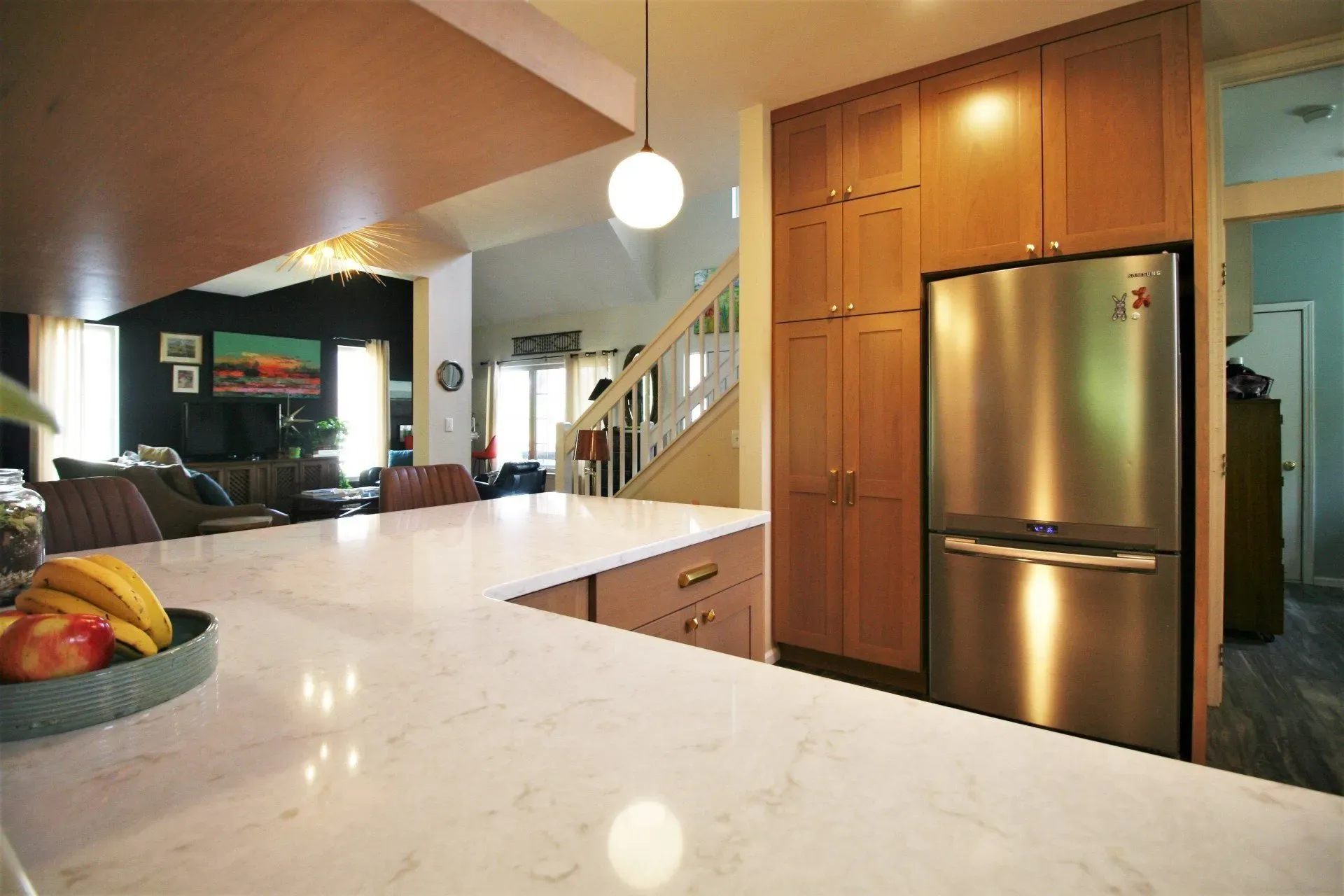 Modern kitchen with marble island, stainless steel fridge, wood cabinets, and open view to living room