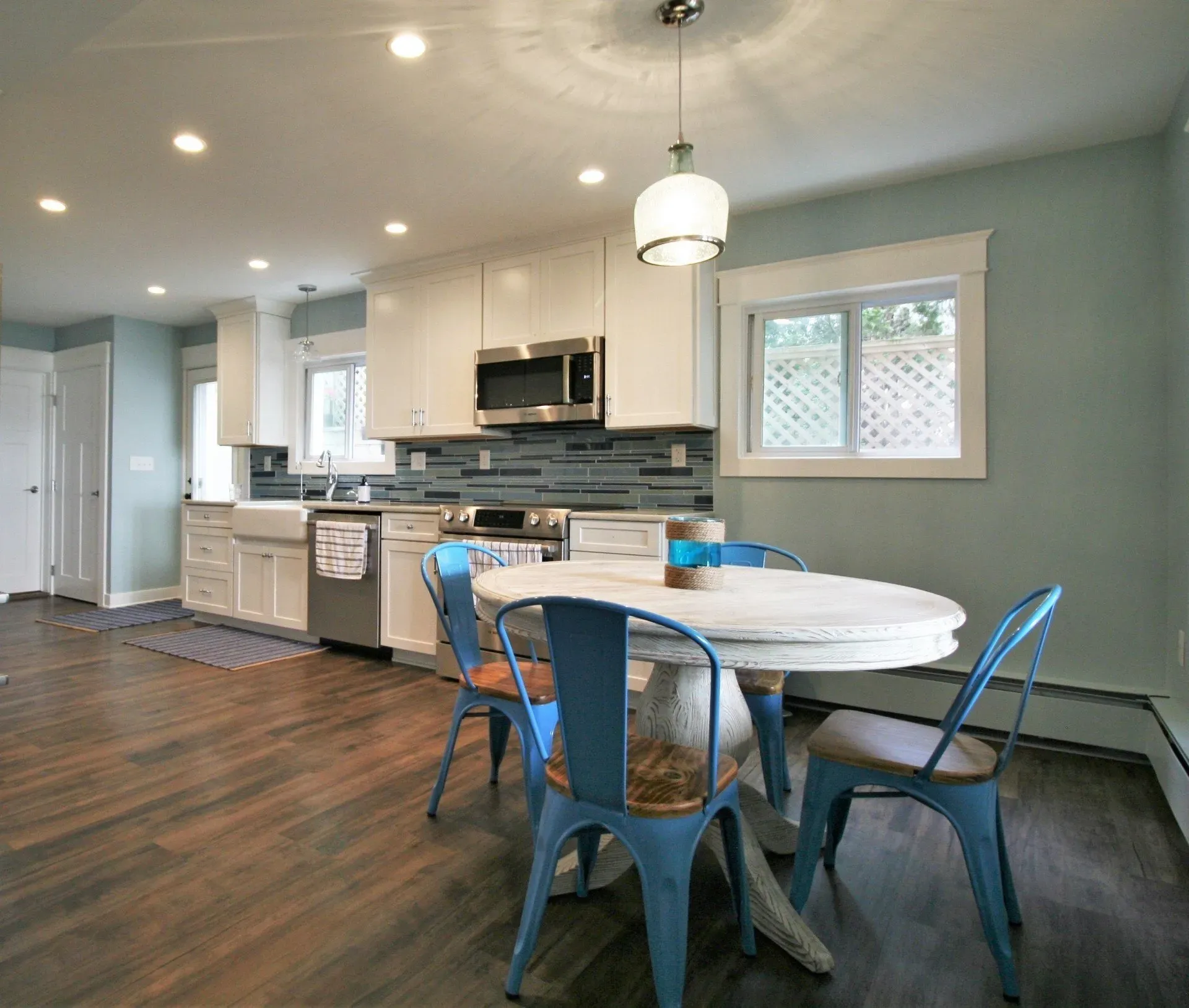 Bright kitchen and dining area with white cabinets, blue chairs, wood floors, and a round table