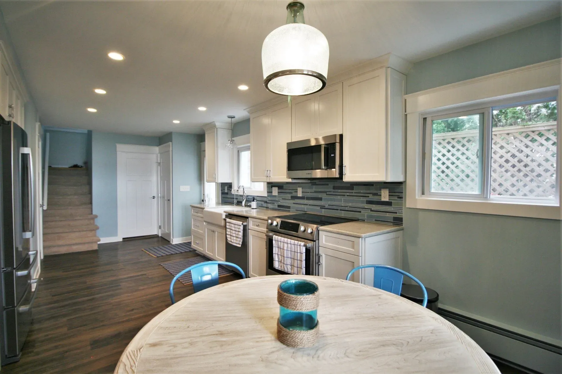 Modern kitchen and dining area with white cabinets, stainless appliances, wood floors, and round table