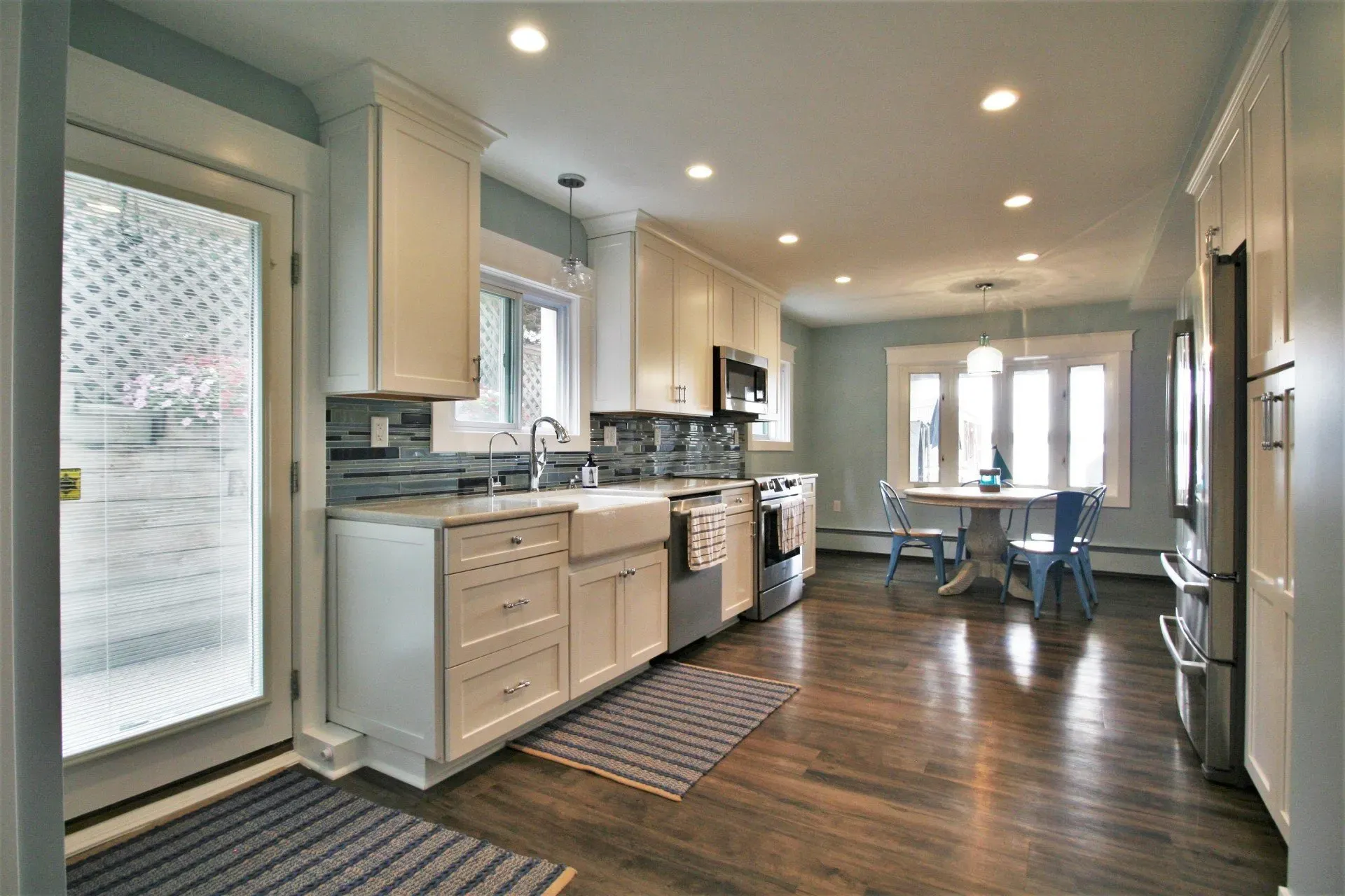 Bright modern kitchen with white cabinets, stainless appliances, dark wood floors, and a small dining table by French doors