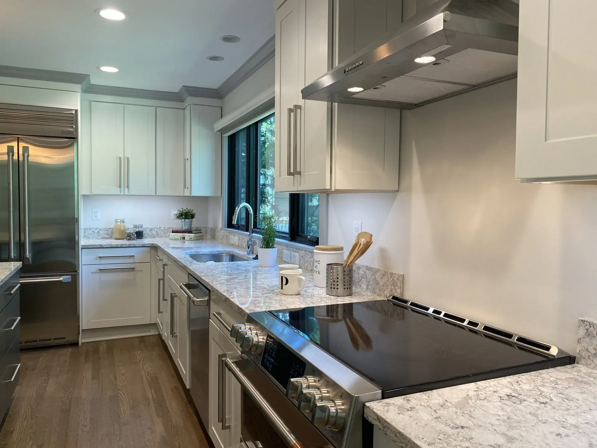 Modern white kitchen with stainless steel appliances, black cooktop, and marble countertops.