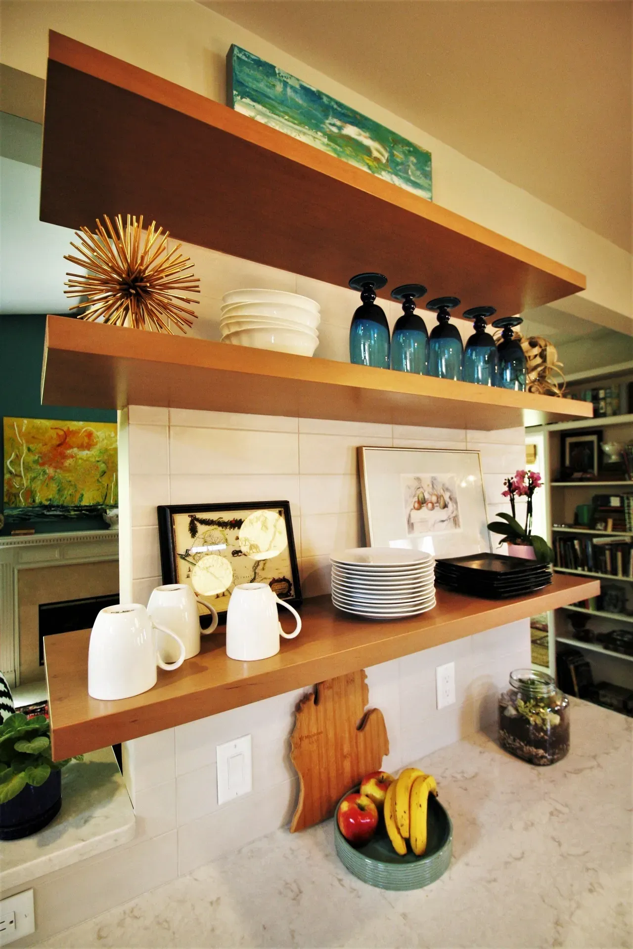 Modern shelf display with dishes, mugs, decor, and bowls of fruit in a kitchen or dining area