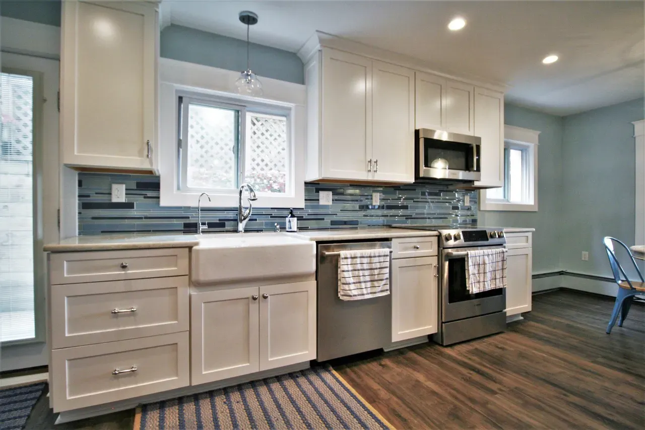 Modern kitchen with white cabinets, stainless appliances, tiled backsplash, and a farmhouse sink