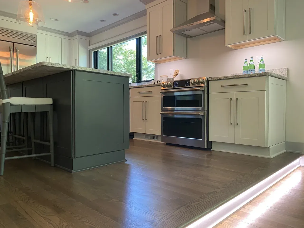 Modern kitchen with island, light cabinets, stainless oven, hardwood floor, and large window.