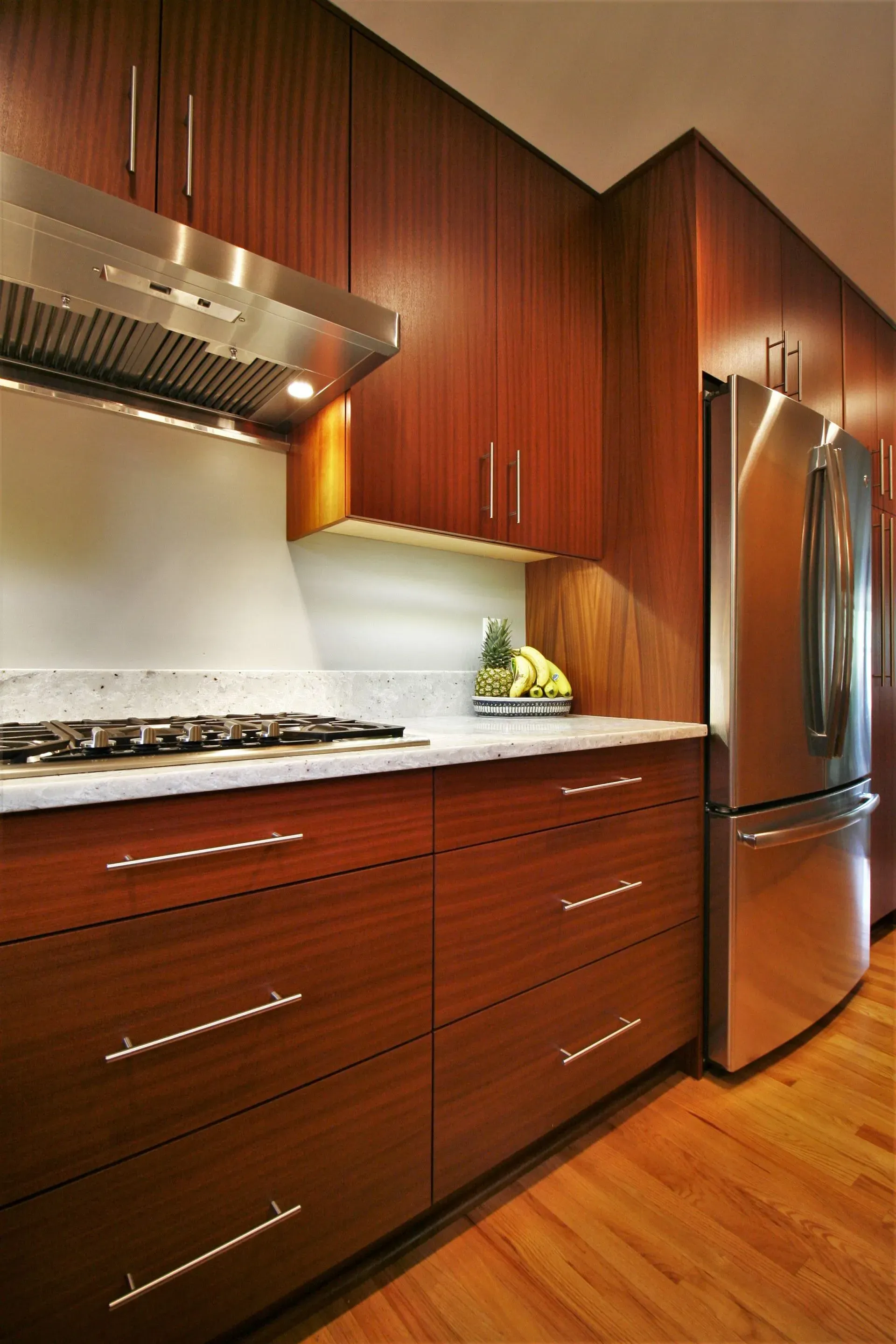 Modern kitchen with dark wood cabinets, stainless steel refrigerator, white backsplash, and hardwood floor