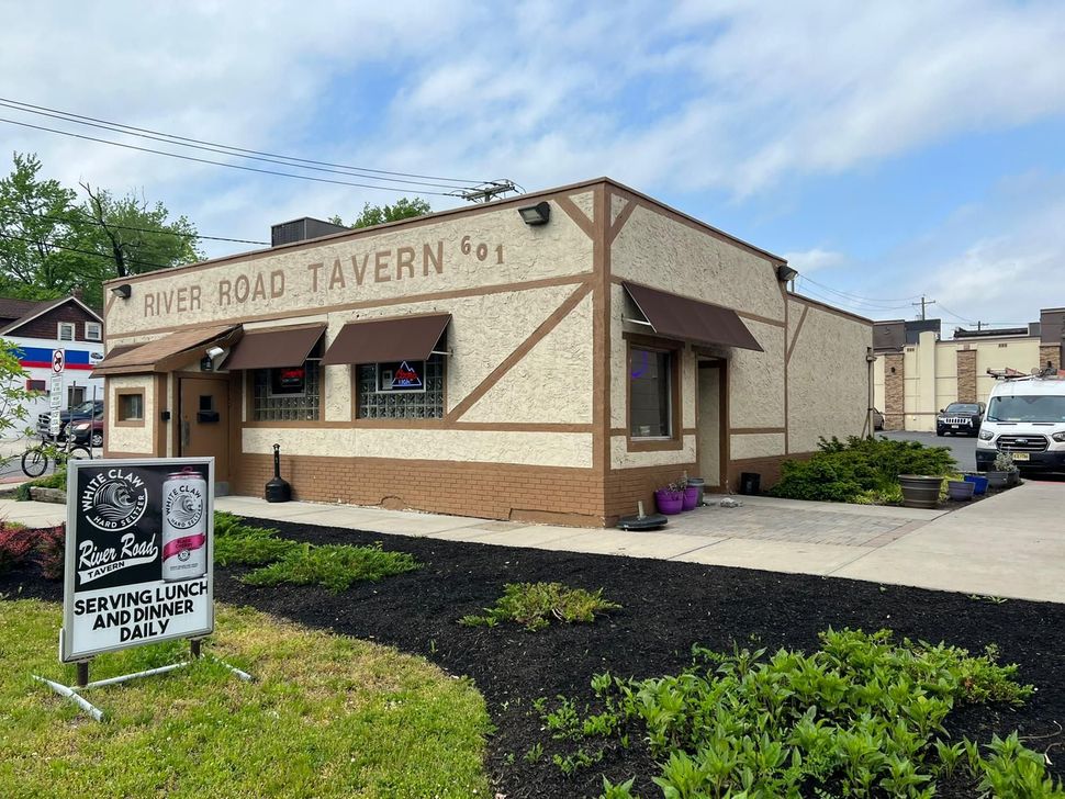 The River Road Tavern storefront with a sidewalk sign and awnings on a partly cloudy day