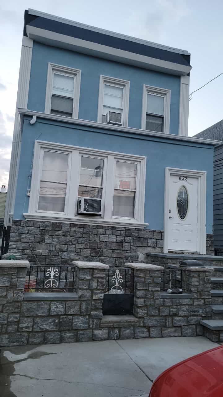 Blue two-story house with white trim, stone front steps, and a white front door on a sloped street